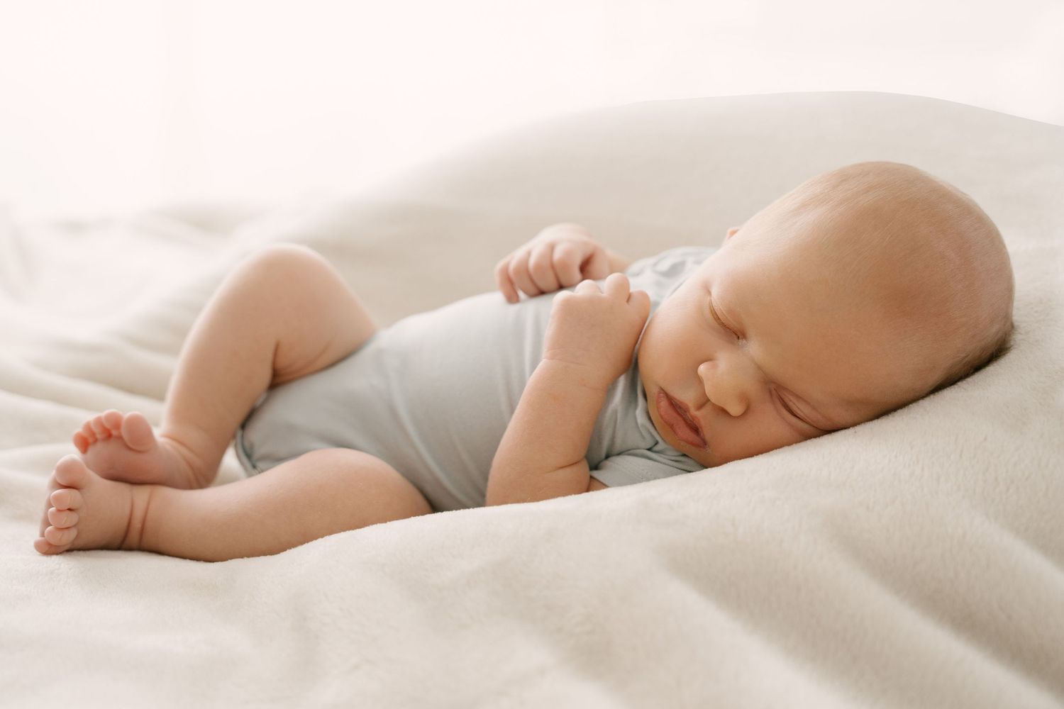 Peaceful newborn baby sleeping on soft white blanket in light onesie.