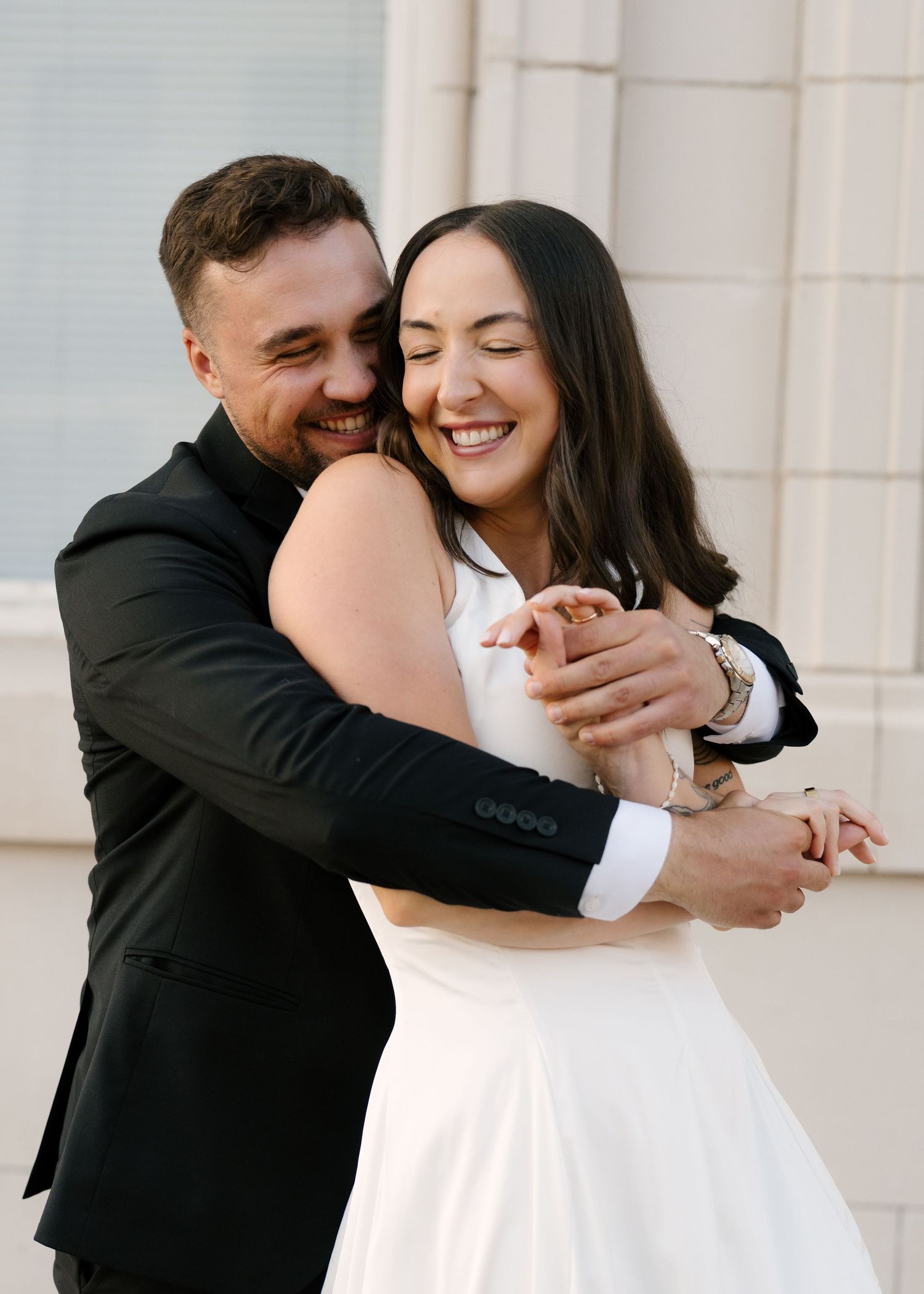 Happy couple sharing a joyful embrace outdoors, bride in white dress and groom in black suit.