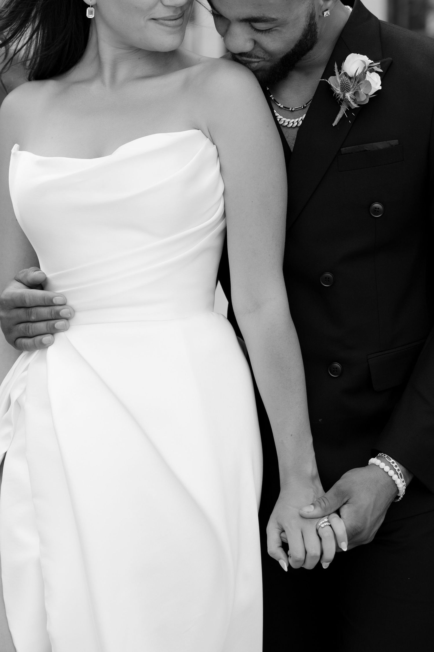 Black and white close-up of bride in strapless white gown and groom in black suit holding hands.