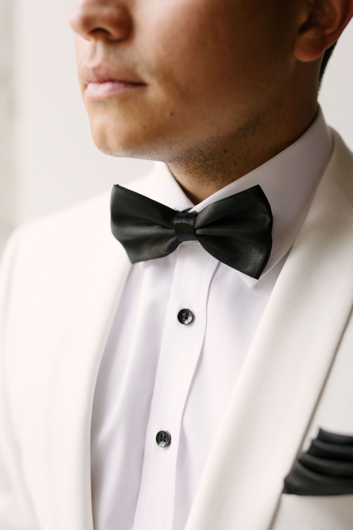 Close-up of groom in white tuxedo jacket with black bow tie and matching pocket square detail.