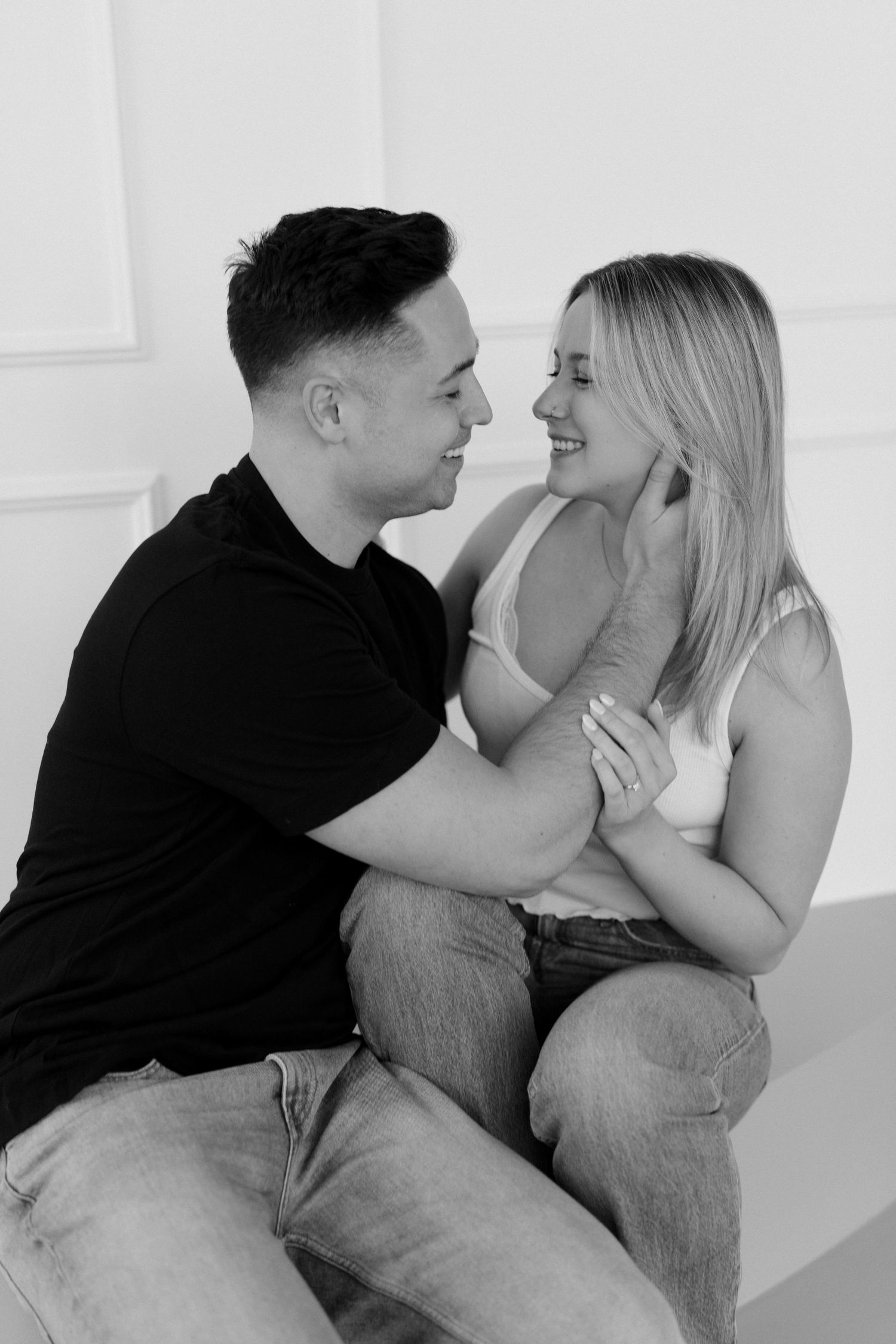 Black and white photo of smiling couple sitting closely together, man gently touching woman's face indoors.