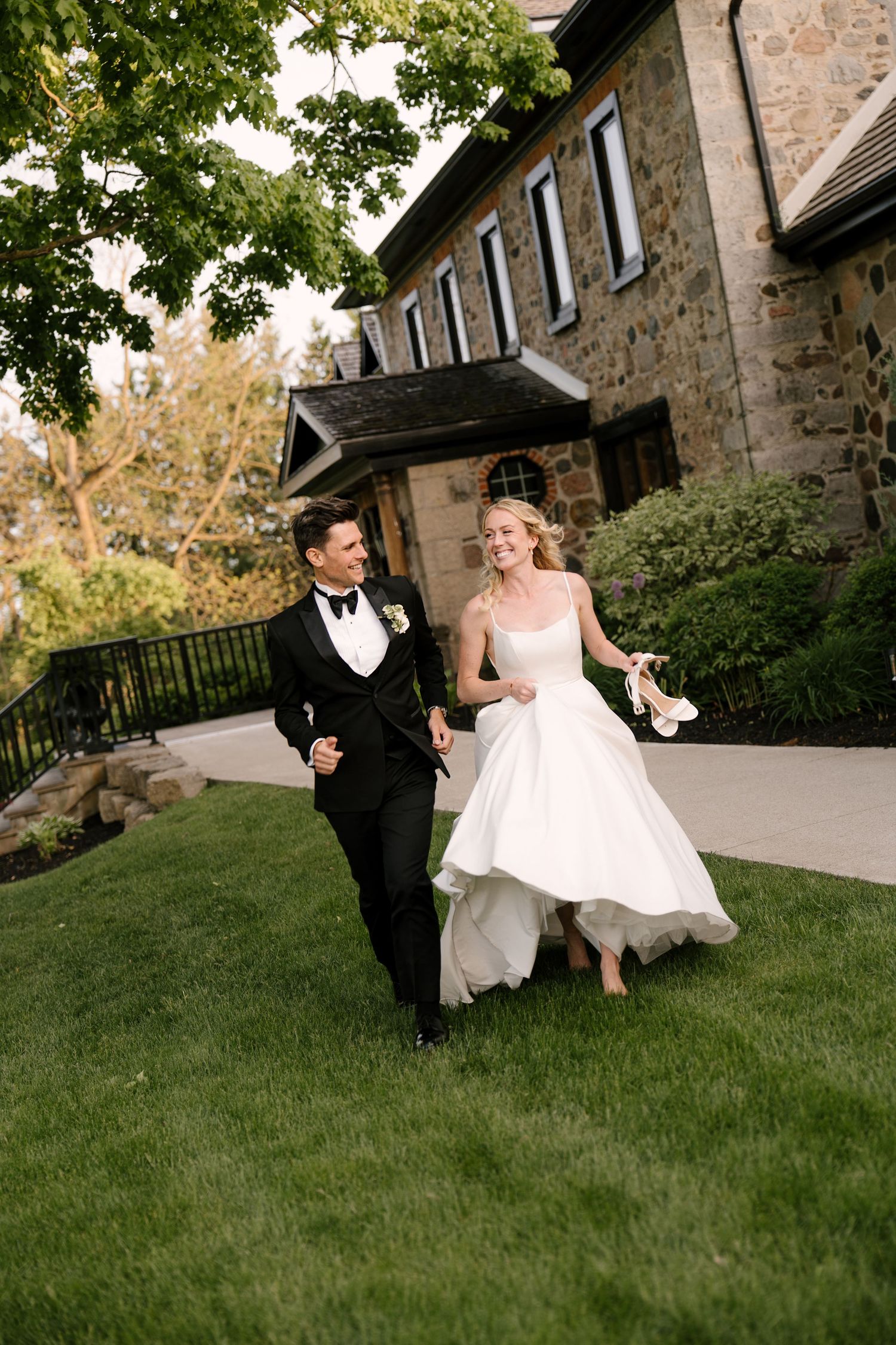 A joyful bride and groom run hand-in-hand across a lush green lawn outside Roseville Estates wedding venue.