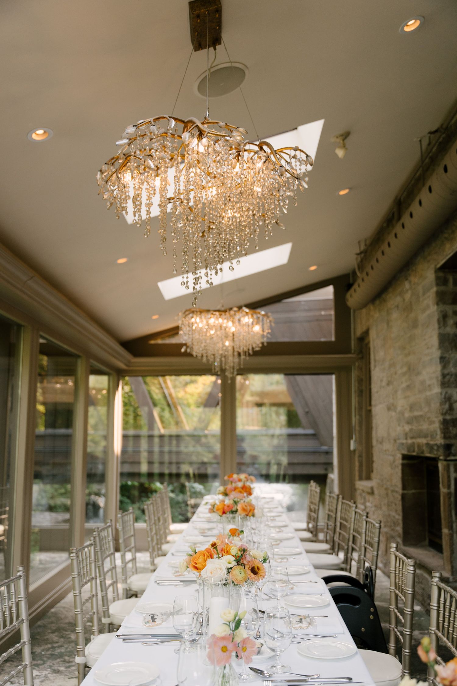 Elegant Ancaster Mill wedding reception table set beneath sparkling crystal chandeliers with orange floral centrepieces.