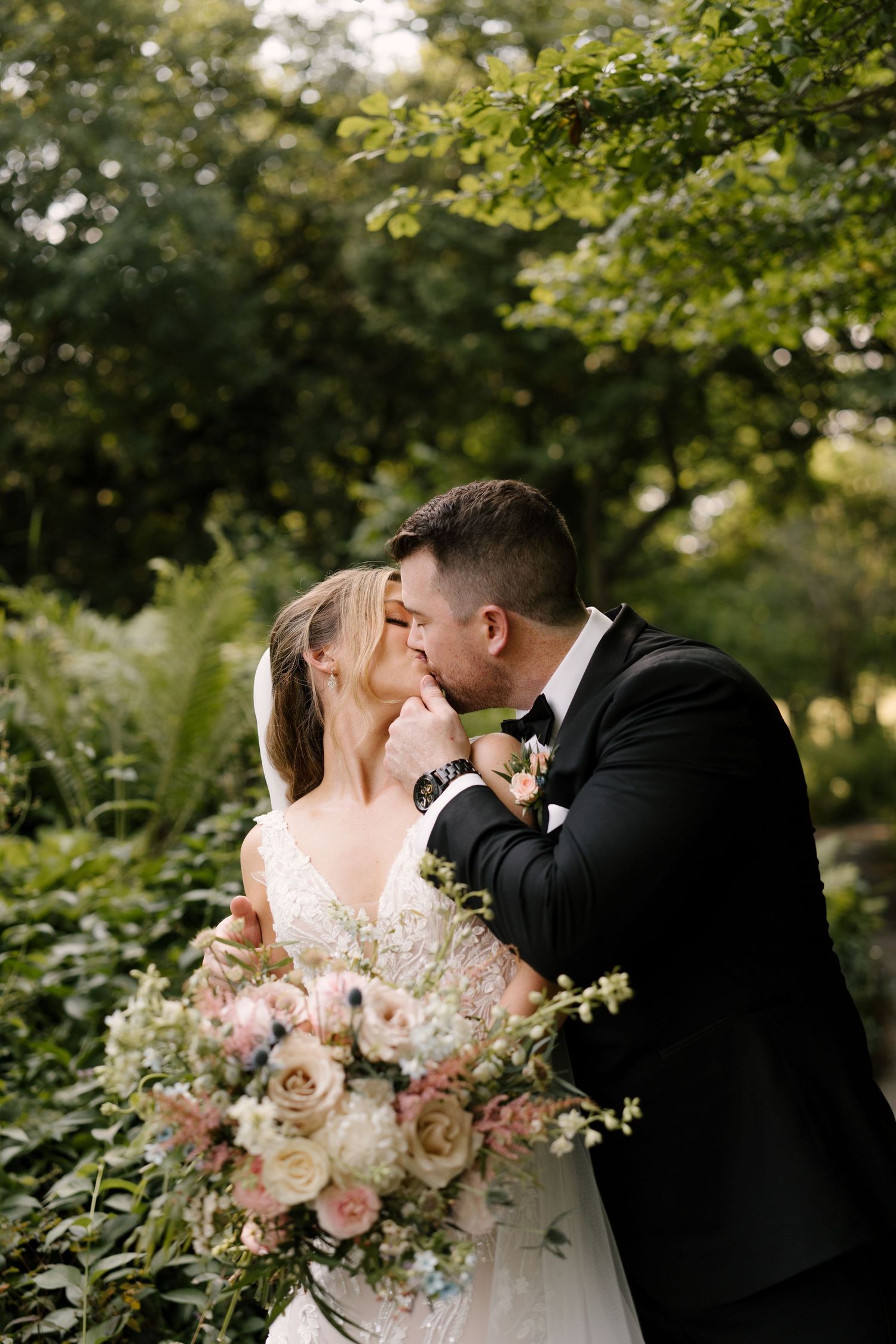Bride and groom sharing a romantic kiss in a garden, bride holding a soft pink and white bouquet at St Marys wedding venue.
