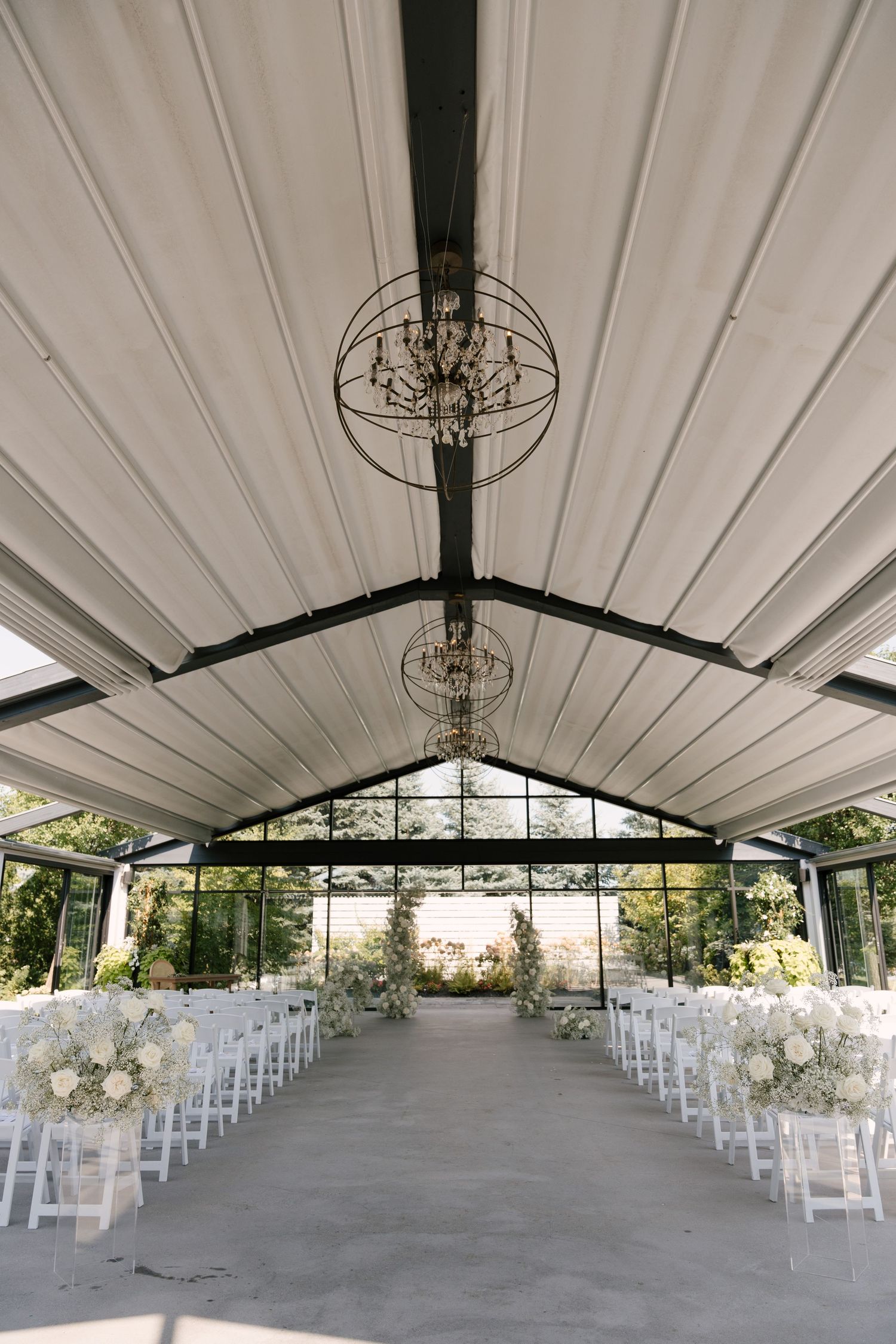 Elegant wedding ceremony venue at Whistle Bear with white chairs, floral arrangements, and chandelier ceiling.