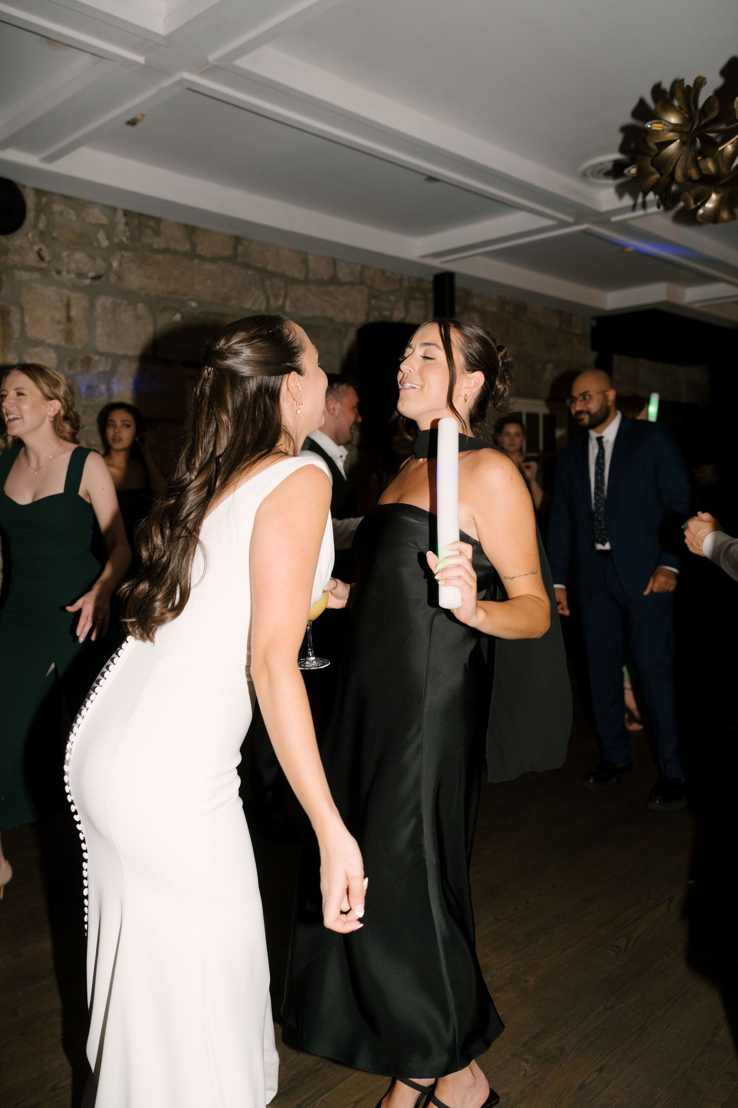 Two women in elegant dresses dancing and laughing together at a wedding reception.
