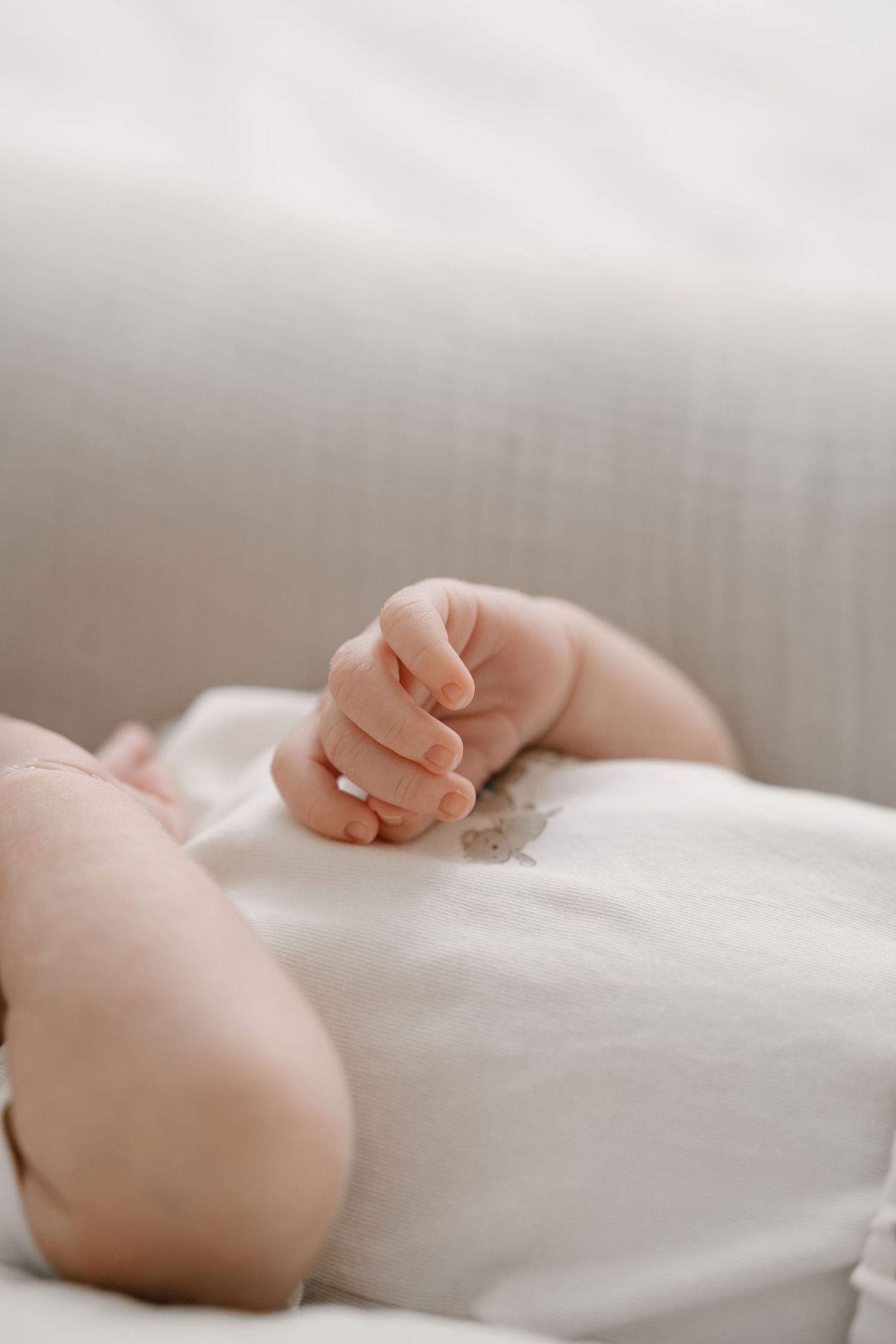 Close-up of peaceful newborn baby fist resting on white blanket.