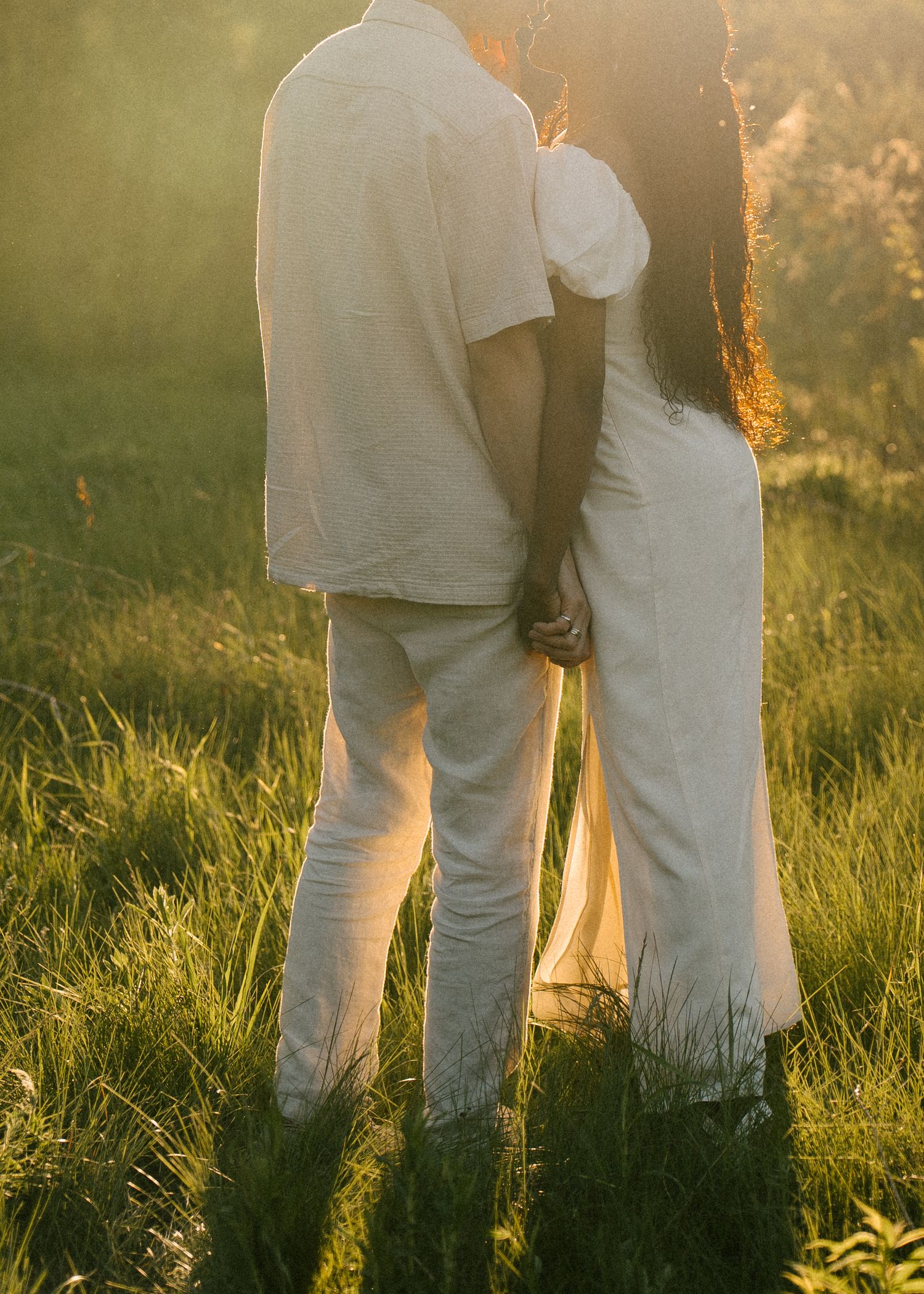 Couple in white outfits holding hands while standing in a sunlit green field.