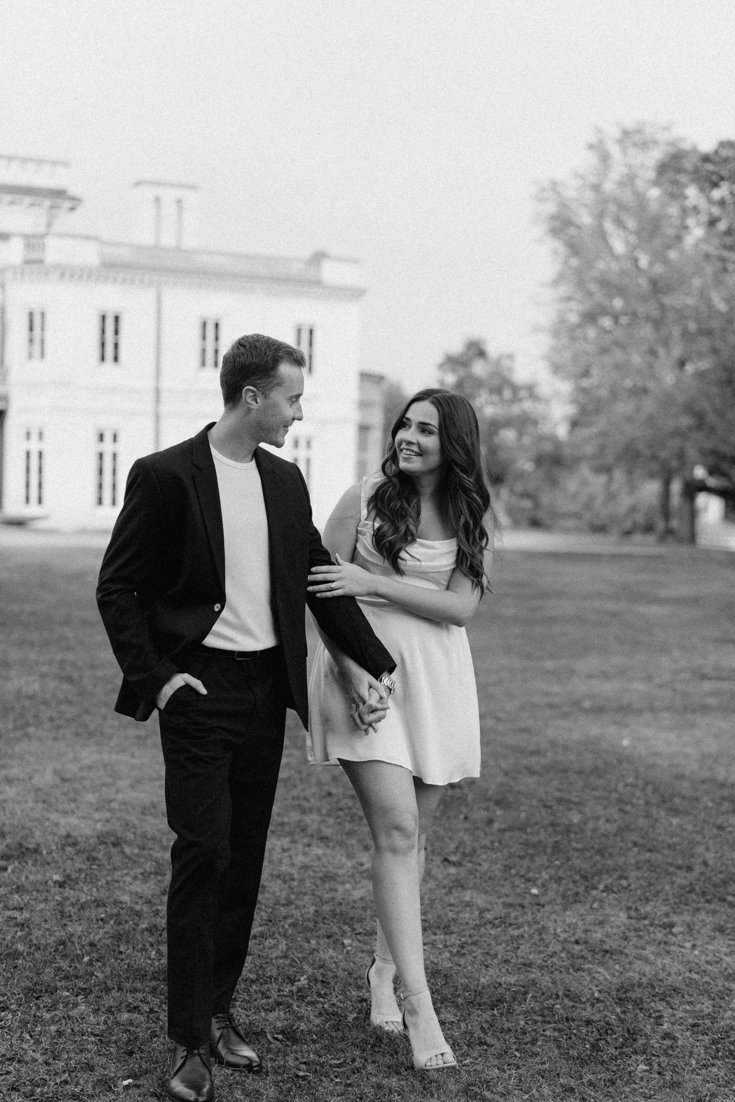 Black and white photo of smiling couple walking arm in arm on estate lawn.