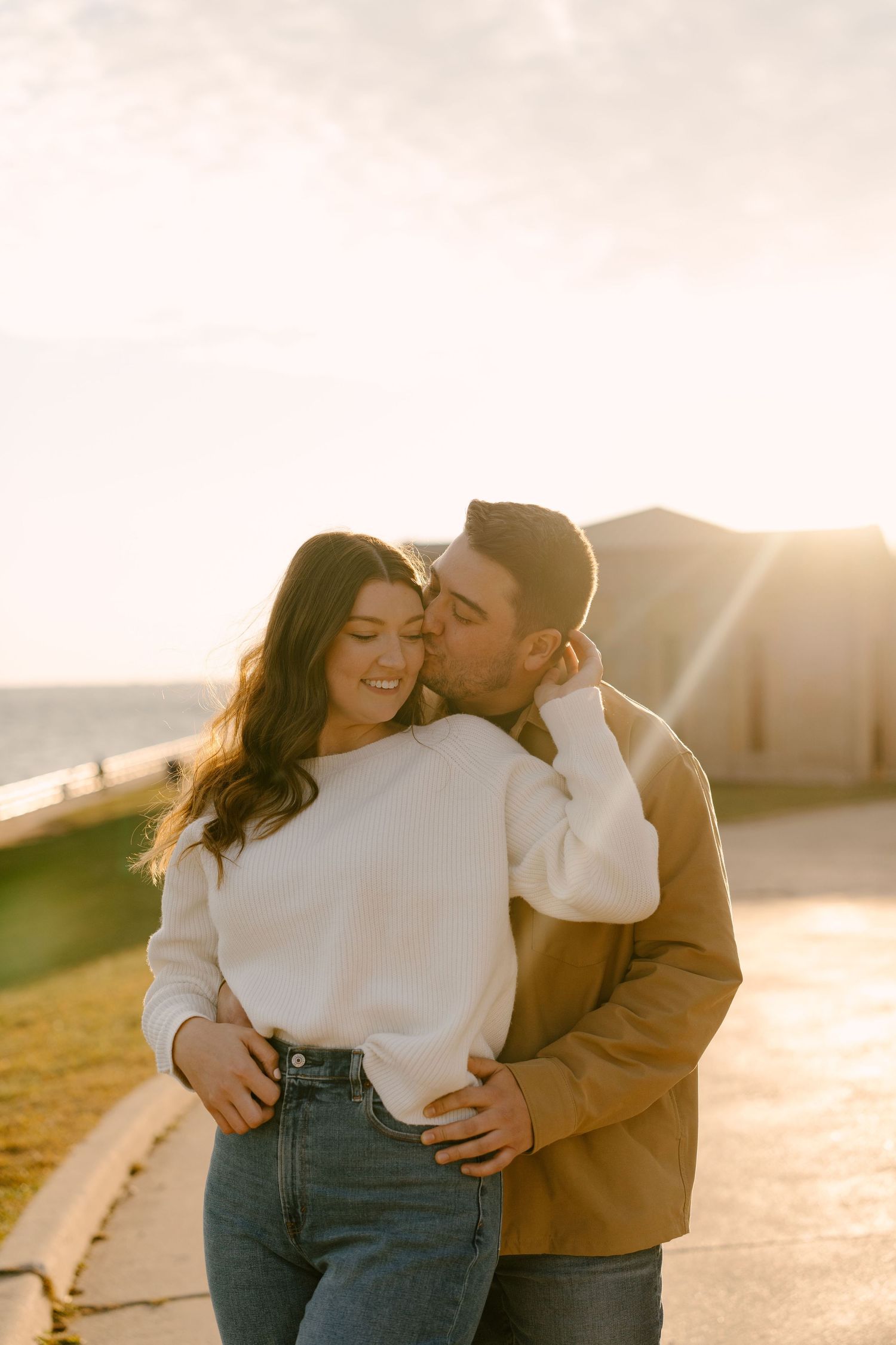 Man kissing smiling woman on cheek during a romantic golden hour outdoor session.
