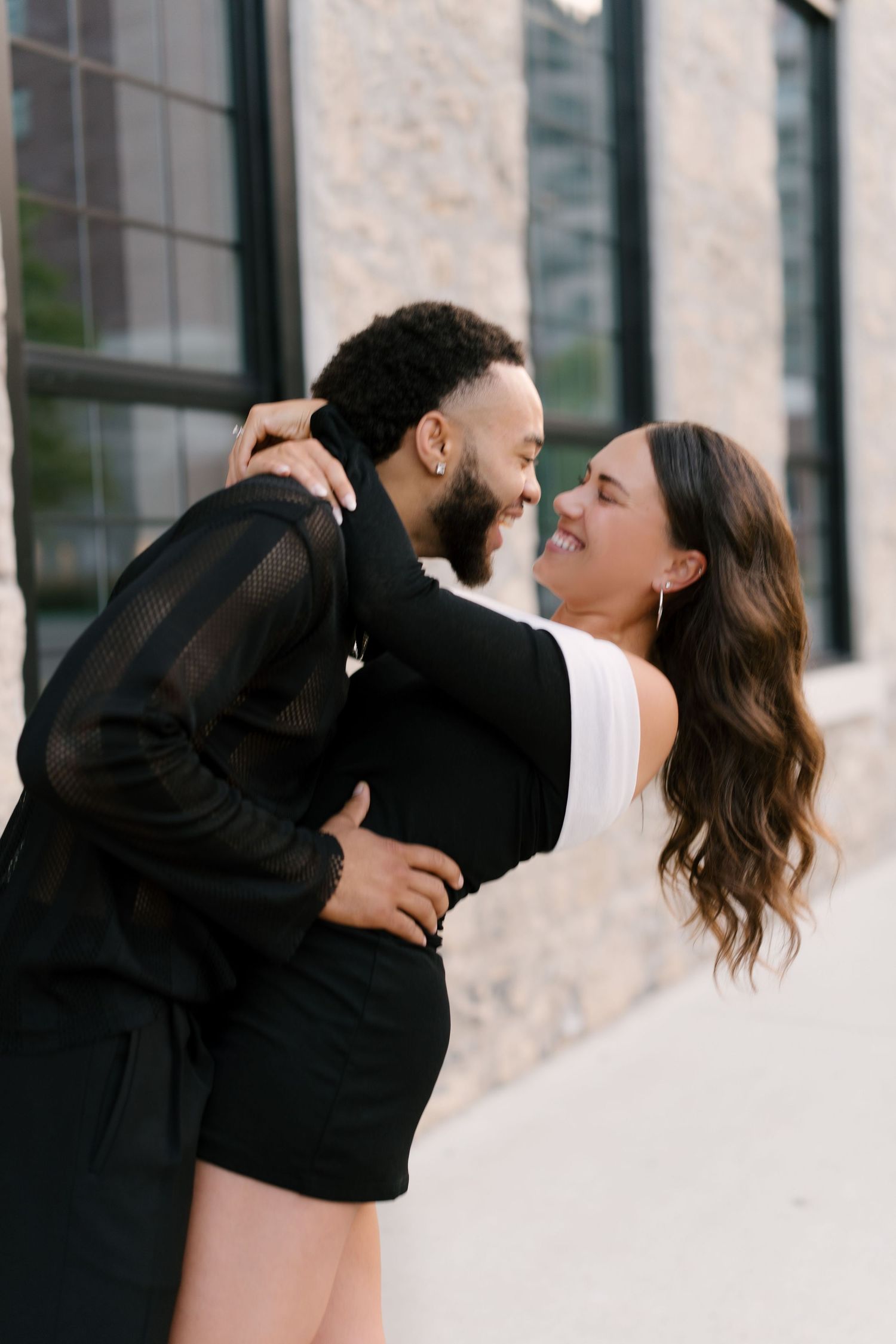Happy couple embracing and laughing together outside a stone building during golden hour.