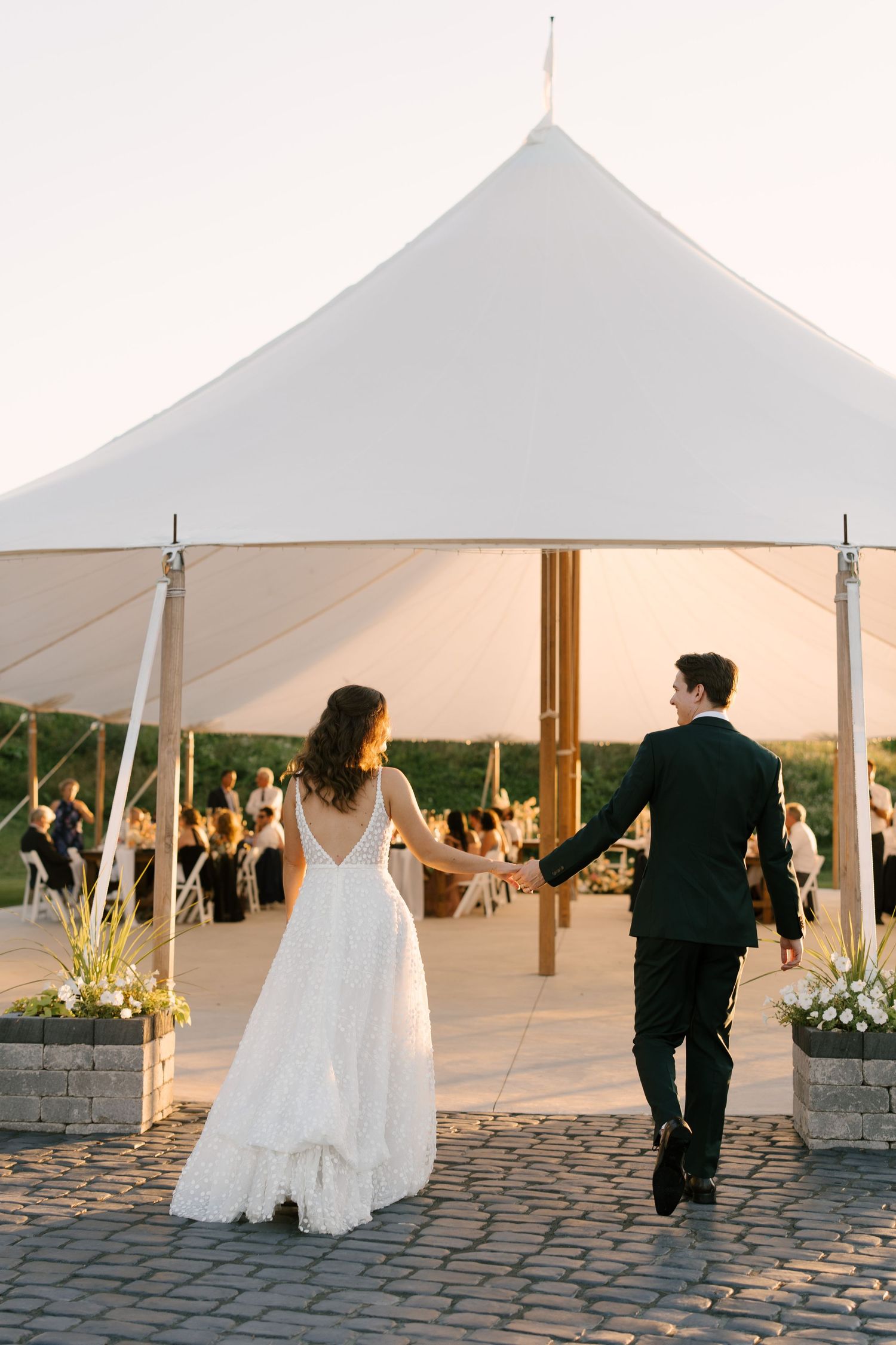 Bride and groom entering outdoor Wakefield Estates wedding reception under elegant white sailcloth tent at dusk.
