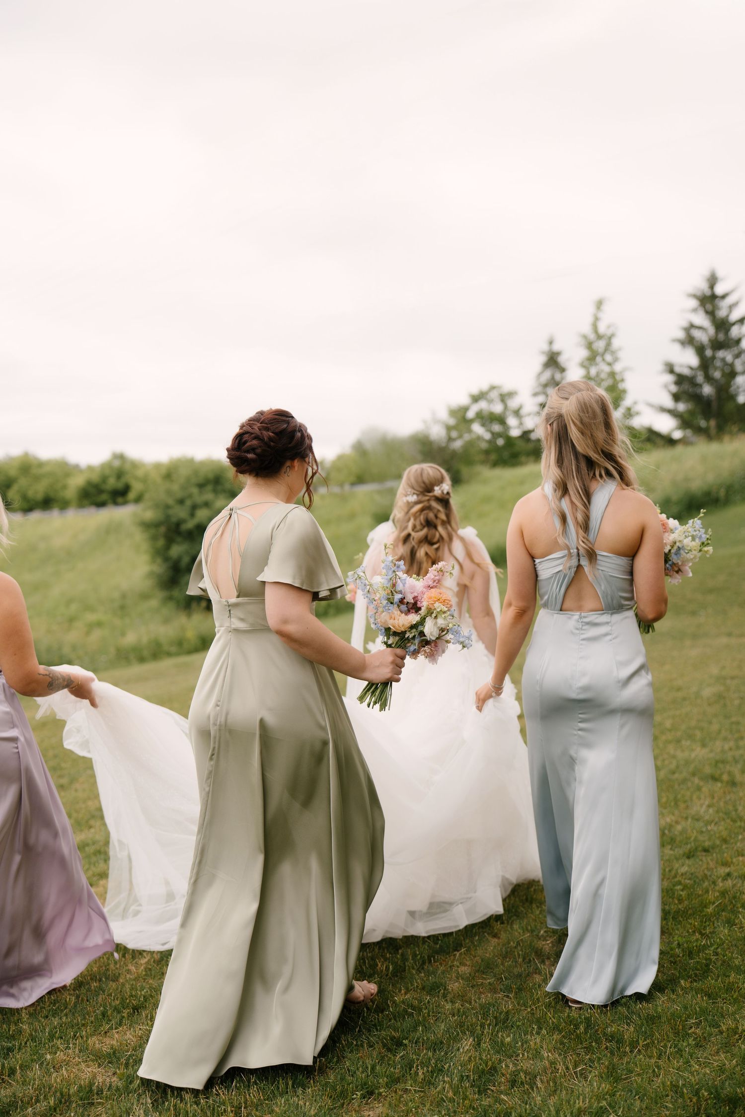 Bridesmaids in sage and blue gowns help carry the brides train across a green lawn at St Marys Golf Club.