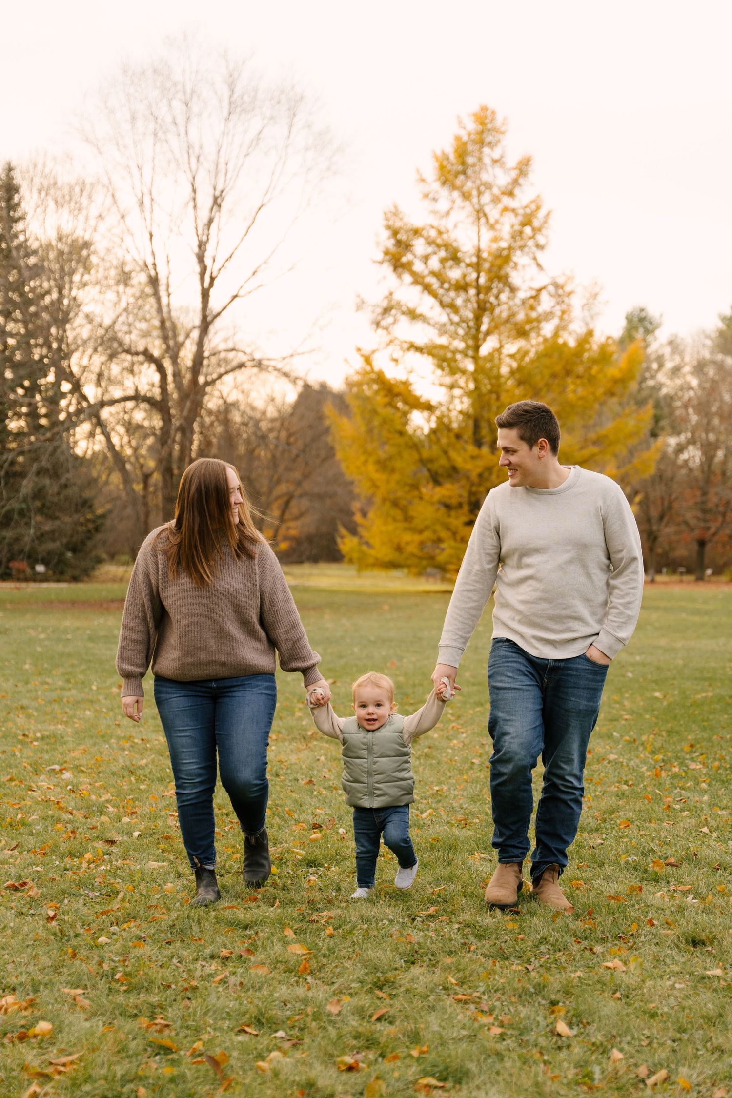 Happy family holding toddler's hands while walking together in colorful autumn park.