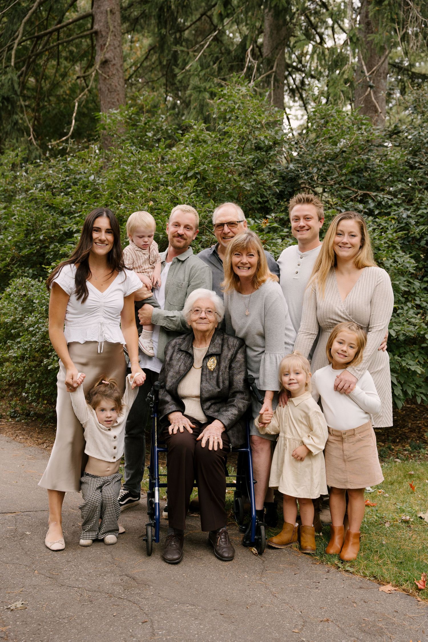 Multi-generational family portrait outdoors with elderly woman in wheelchair at center.