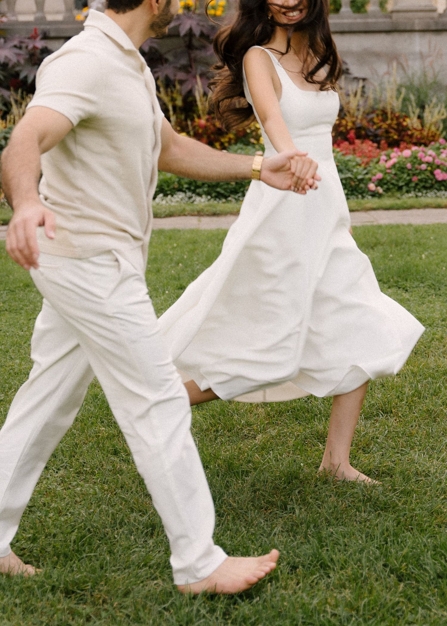 Barefoot couple dancing and spinning joyfully on green grass in coordinating white outfits outdoors.