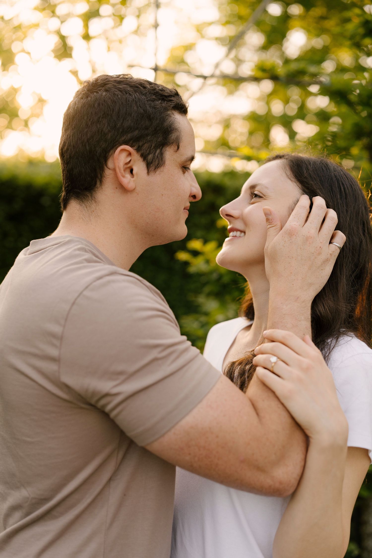 Couple gazing lovingly at each other outdoors at sunset, man gently brushing woman's hair from her face.