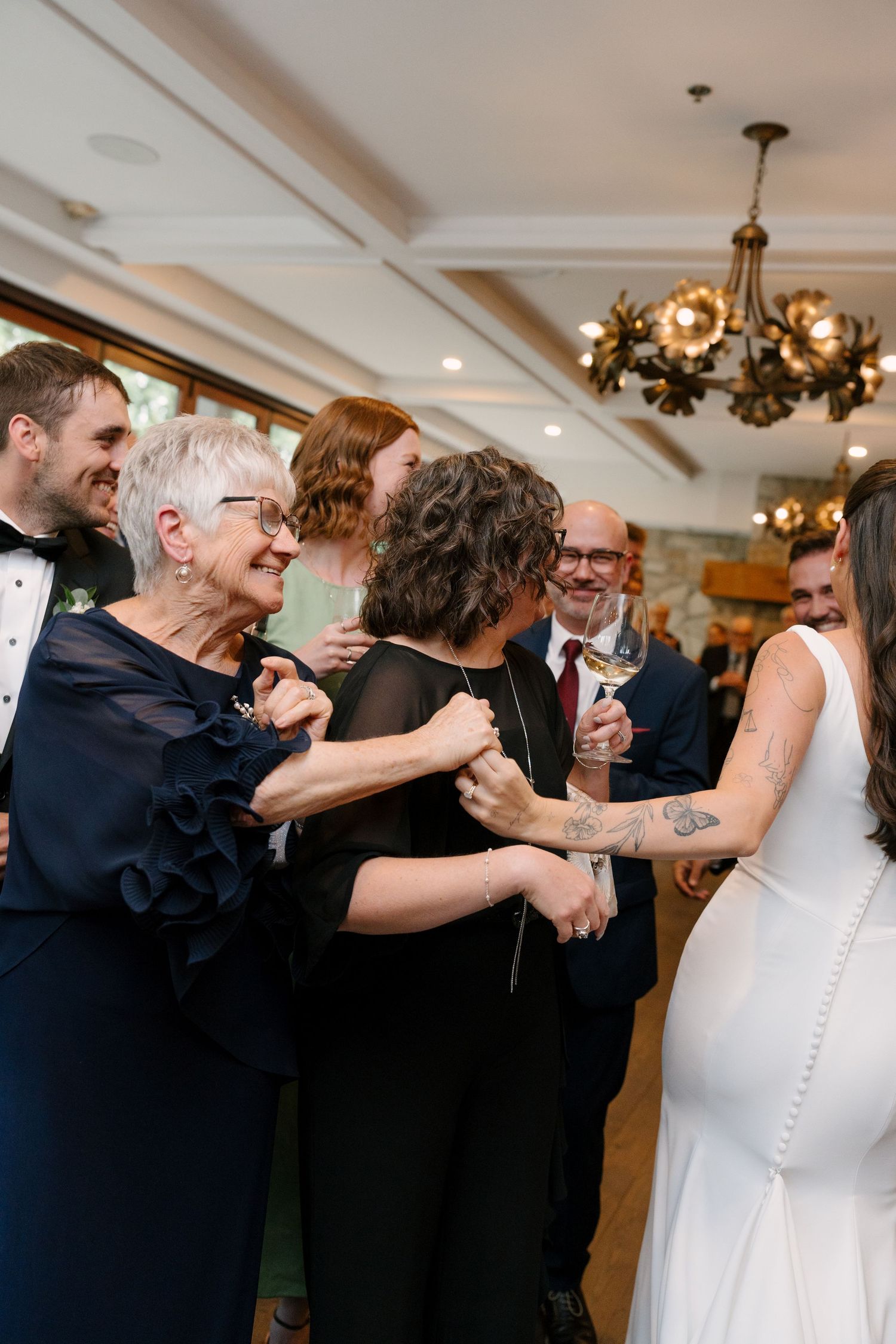 Bride in white gown greeting elderly guests on dance floor at elegant wedding reception with gold chandelier.