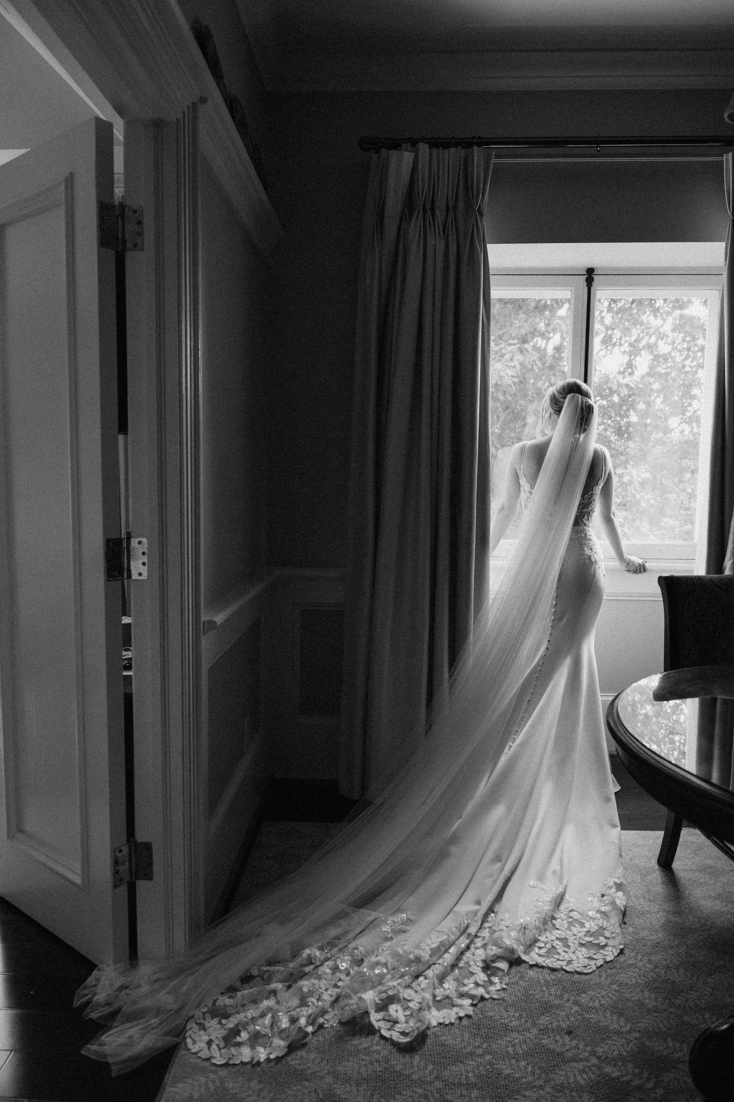 Black and white bridal portrait of a bride in a lace-trimmed cathedral veil gown by a window at Langdon hall wedding venue.