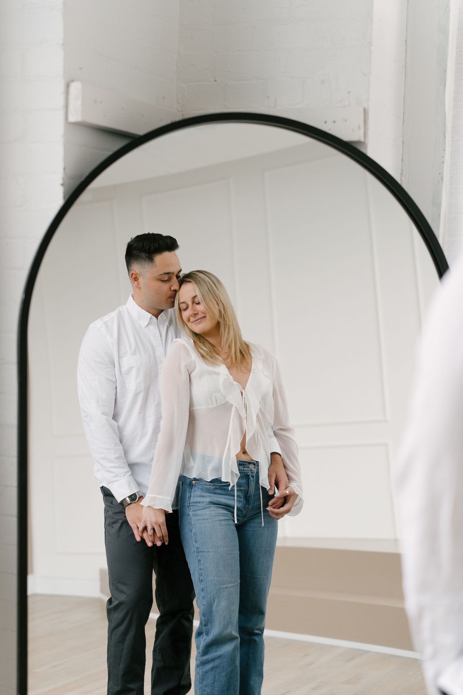 Couple sharing tender kiss reflected in large arch mirror.