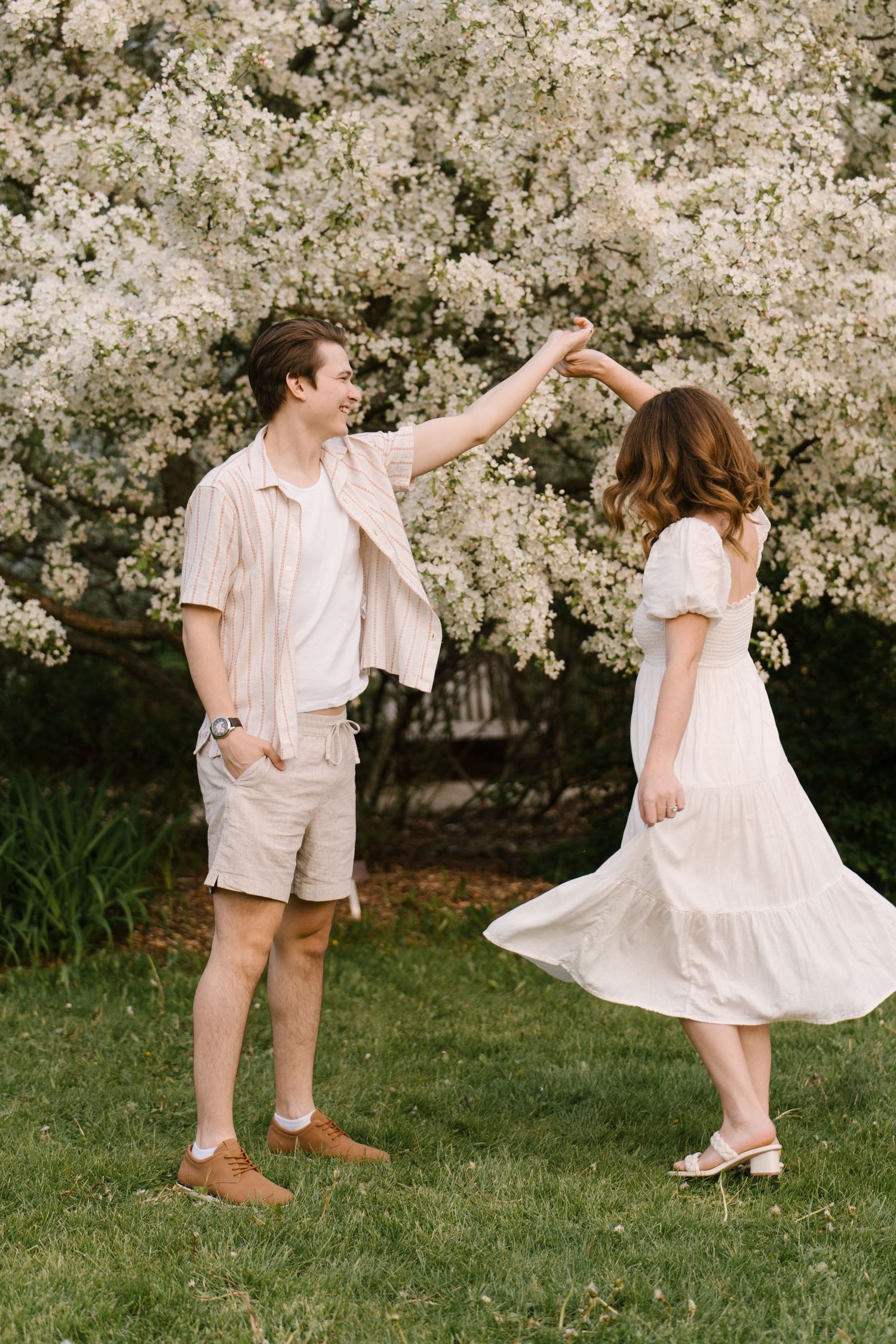 Happy couple dancing together on a green lawn in front of a beautiful white flowering tree in spring.
