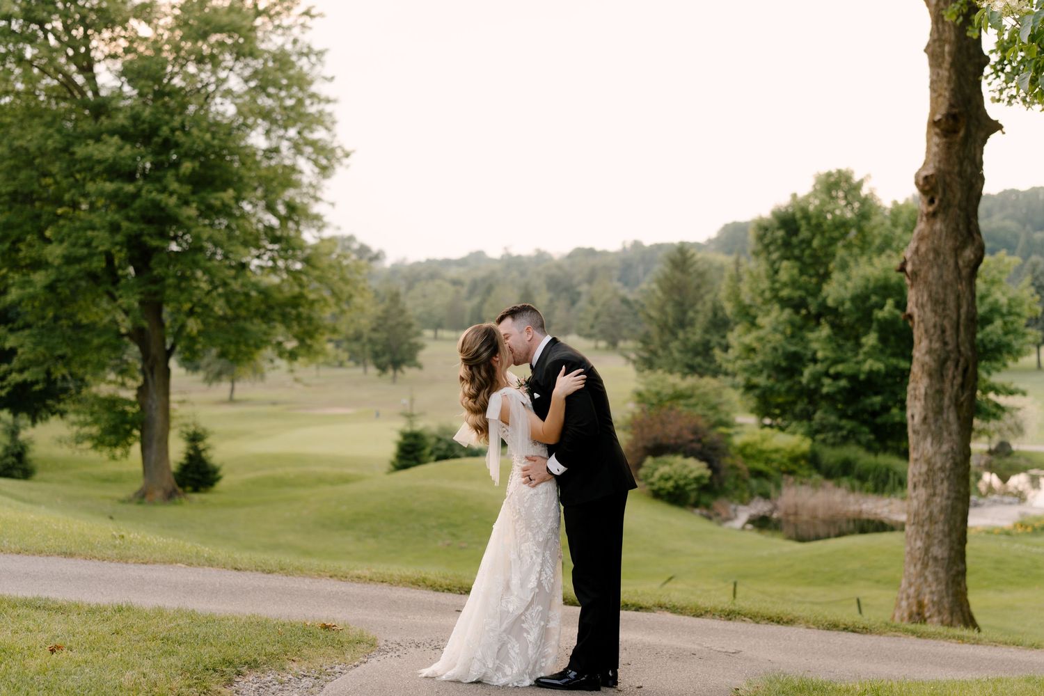 Bride and groom sharing a romantic kiss on a tree-lined path at an outdoor St Marys Golf Club wedding venue.