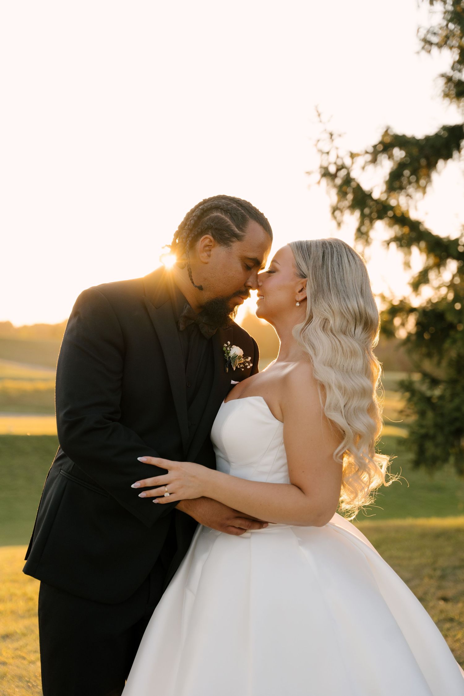 Bride and groom share an intimate moment at golden hour on a golf course, her white ballgown glowing.