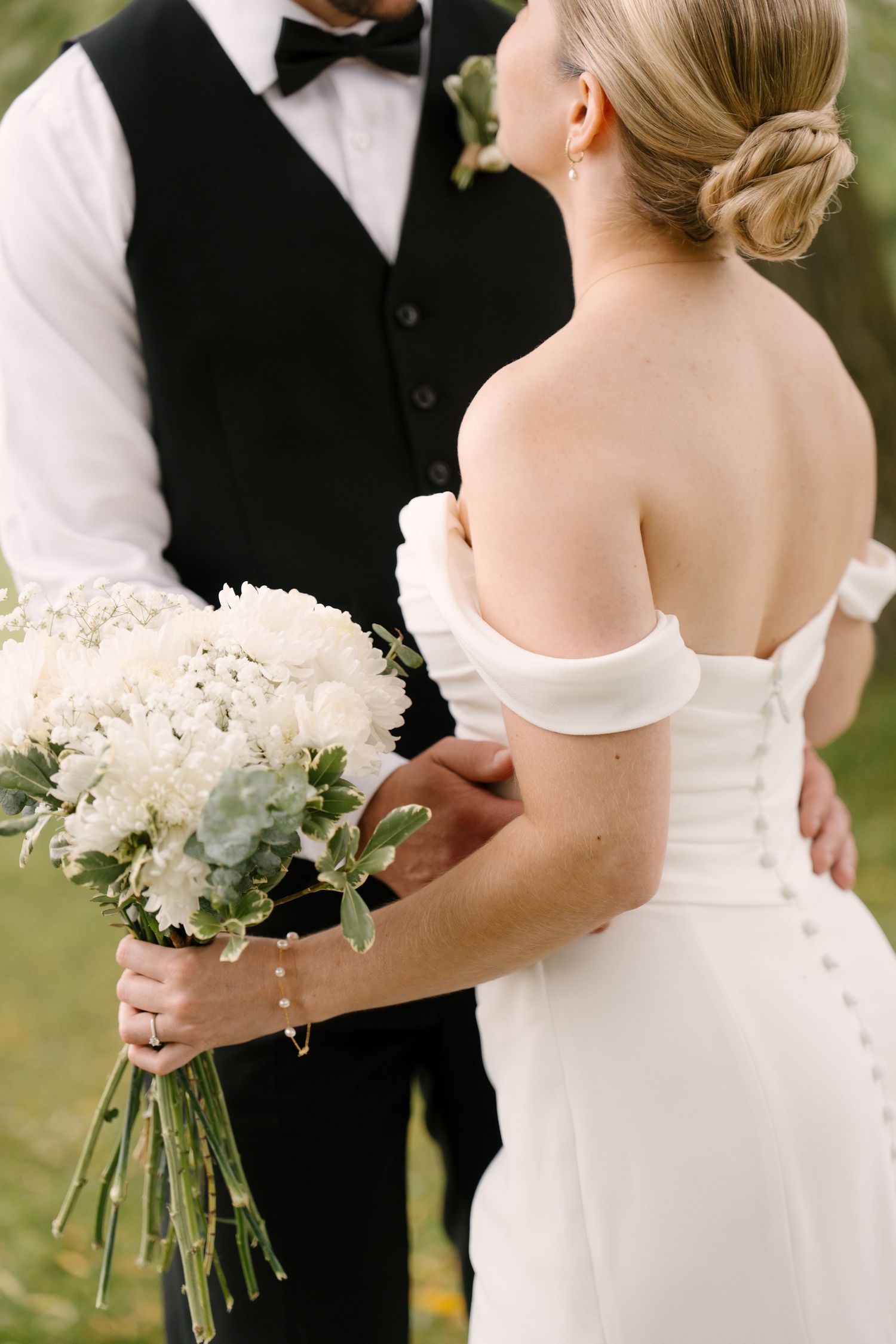 Close-up of bride in off-shoulder gown with button back holding white wedding bouquet.