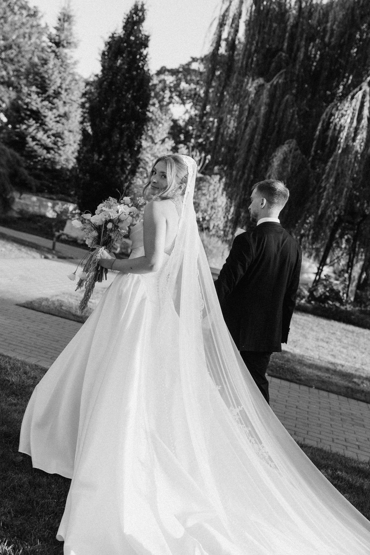 Bride and groom walking in a garden, bride in flowing gown with long veil and bouquet at Pillar and Post.