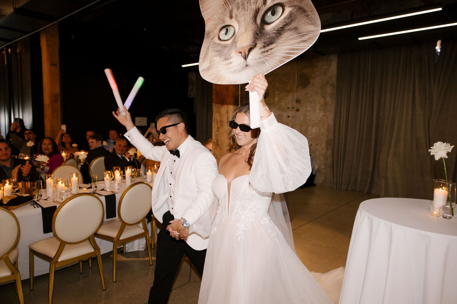 Bride and groom making fun entrance with giant cat balloon and glow sticks at reception in Tapestry Hall.