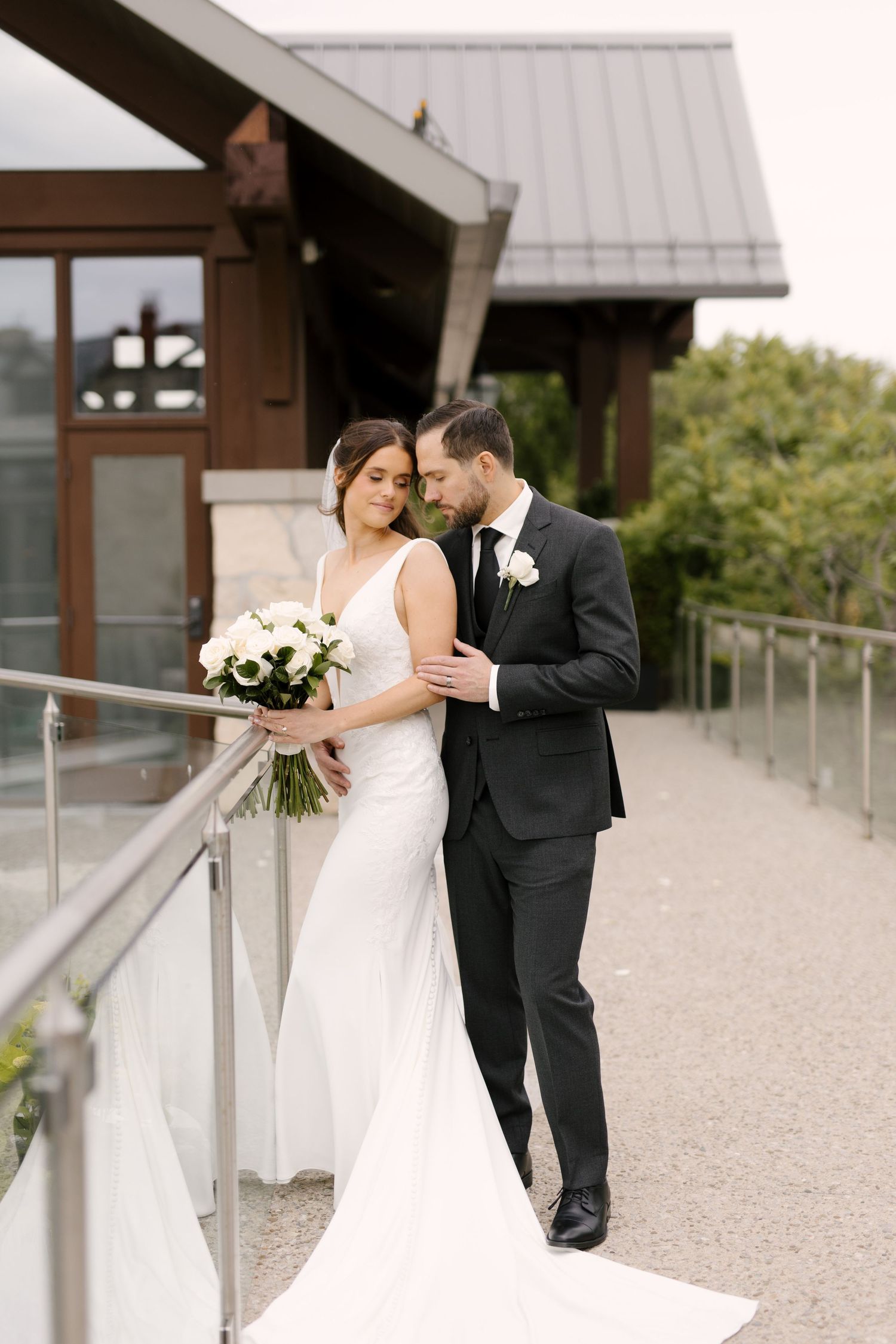 Bride and groom share intimate moment on outdoor Cambridge Mill terrace, bride holding white floral bouquet in elegant gown.
