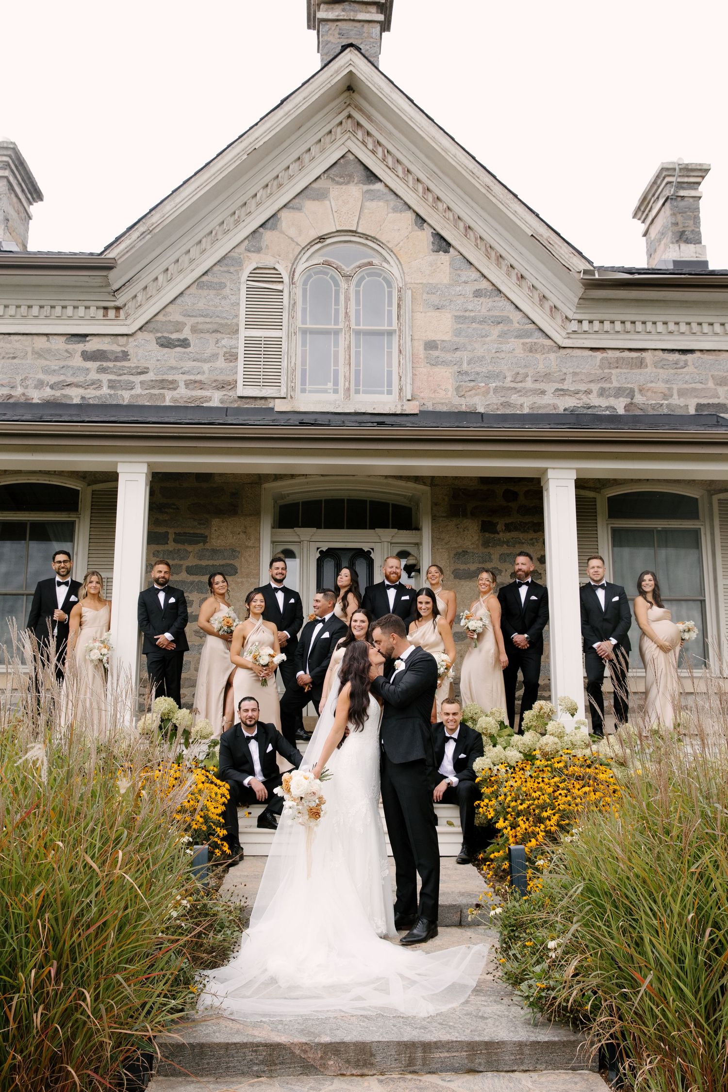 Wedding party posing on steps of a historic stone mansion with floral arrangements.