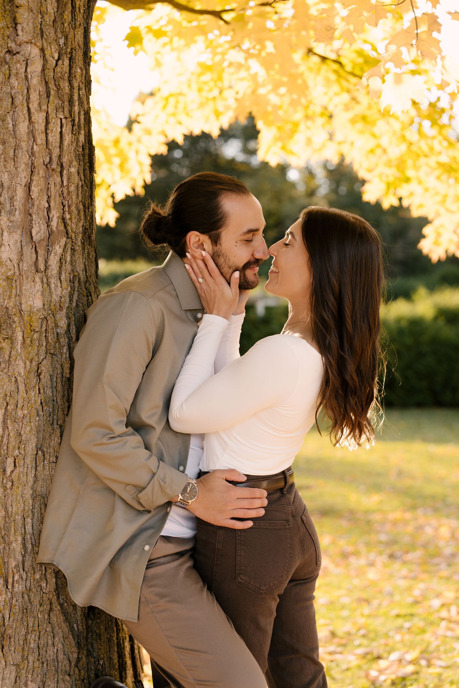 Romantic couple sharing an intimate moment leaning against a tree with golden fall foliage.
