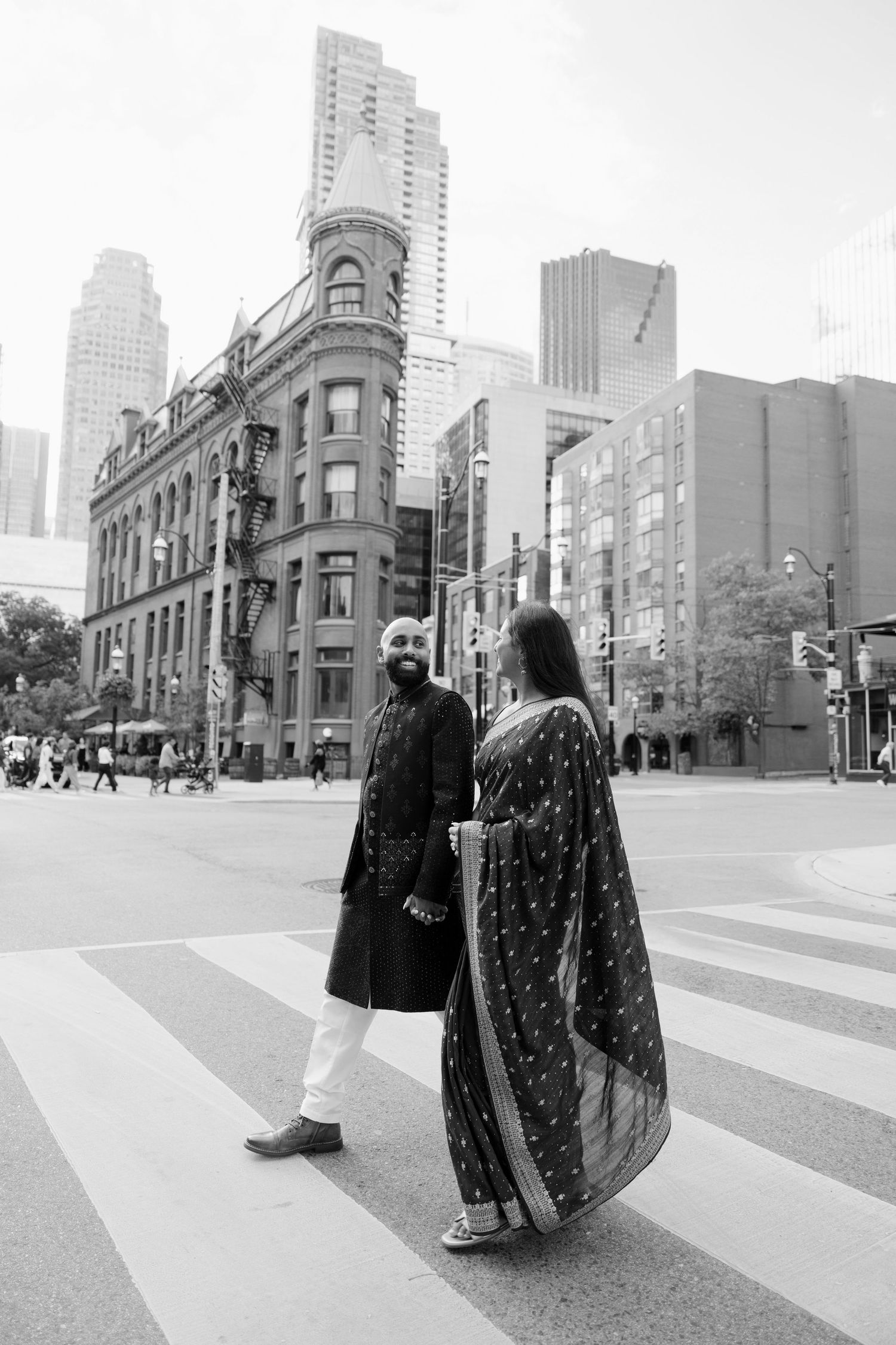 Indian couple in traditional attire cross street near Toronto Gooderham Flatiron Building.