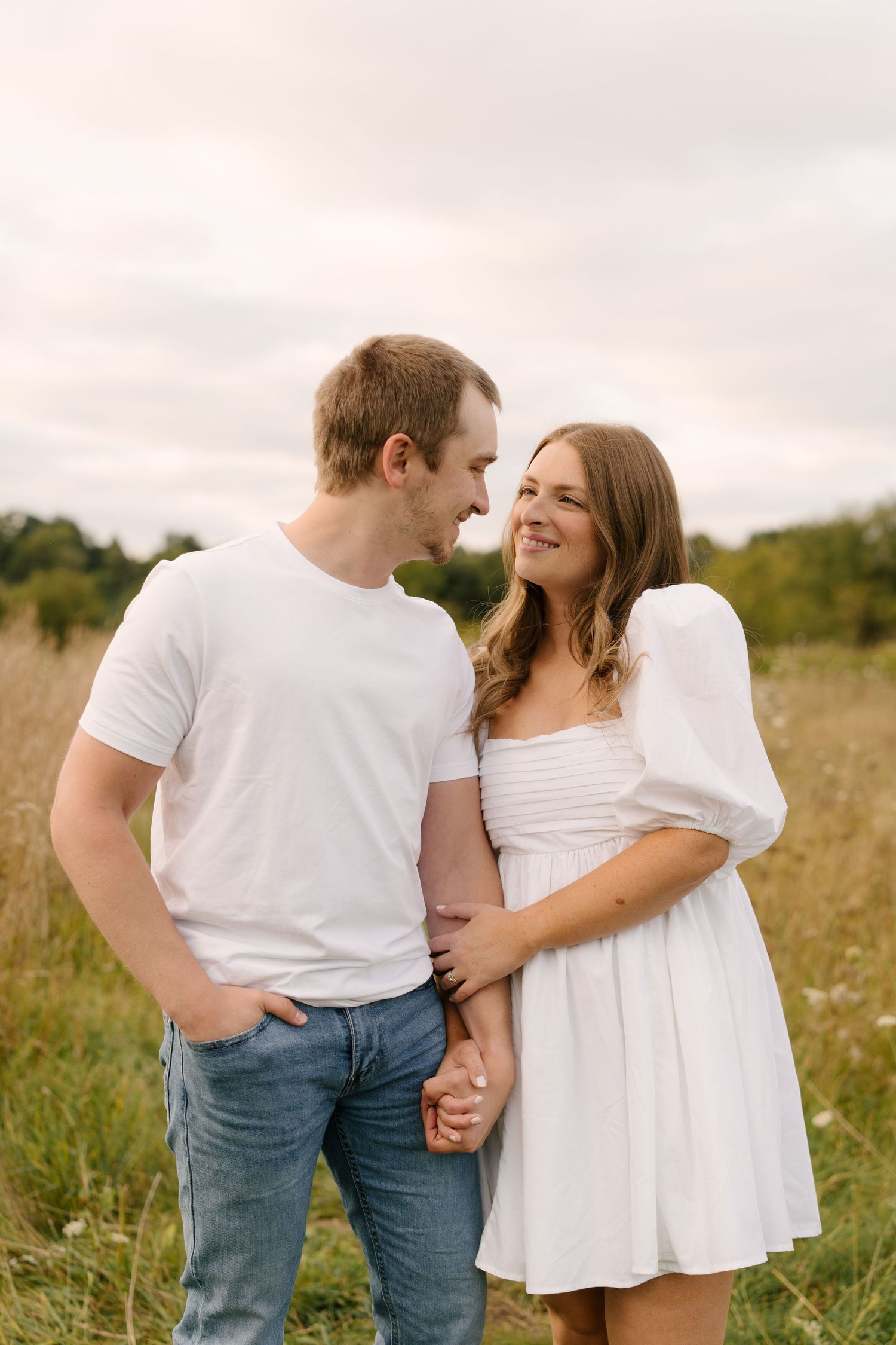 Couple holding hands and gazing at each other lovingly in an open grassy field.