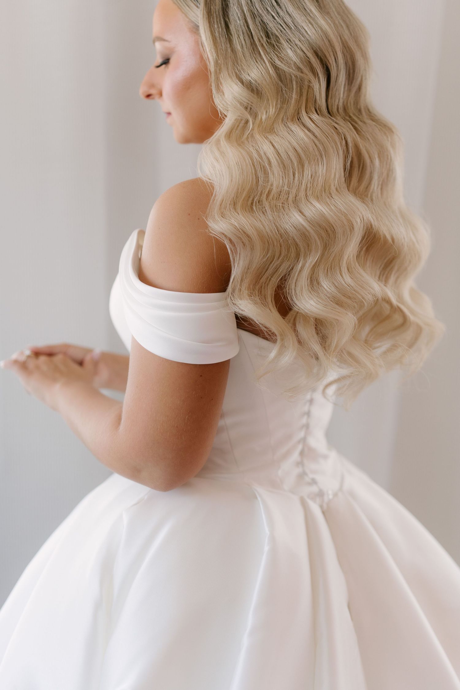 Blonde bride in off-shoulder white corset ballgown showing elegant back detail with curled hair in The Walper Hotel.