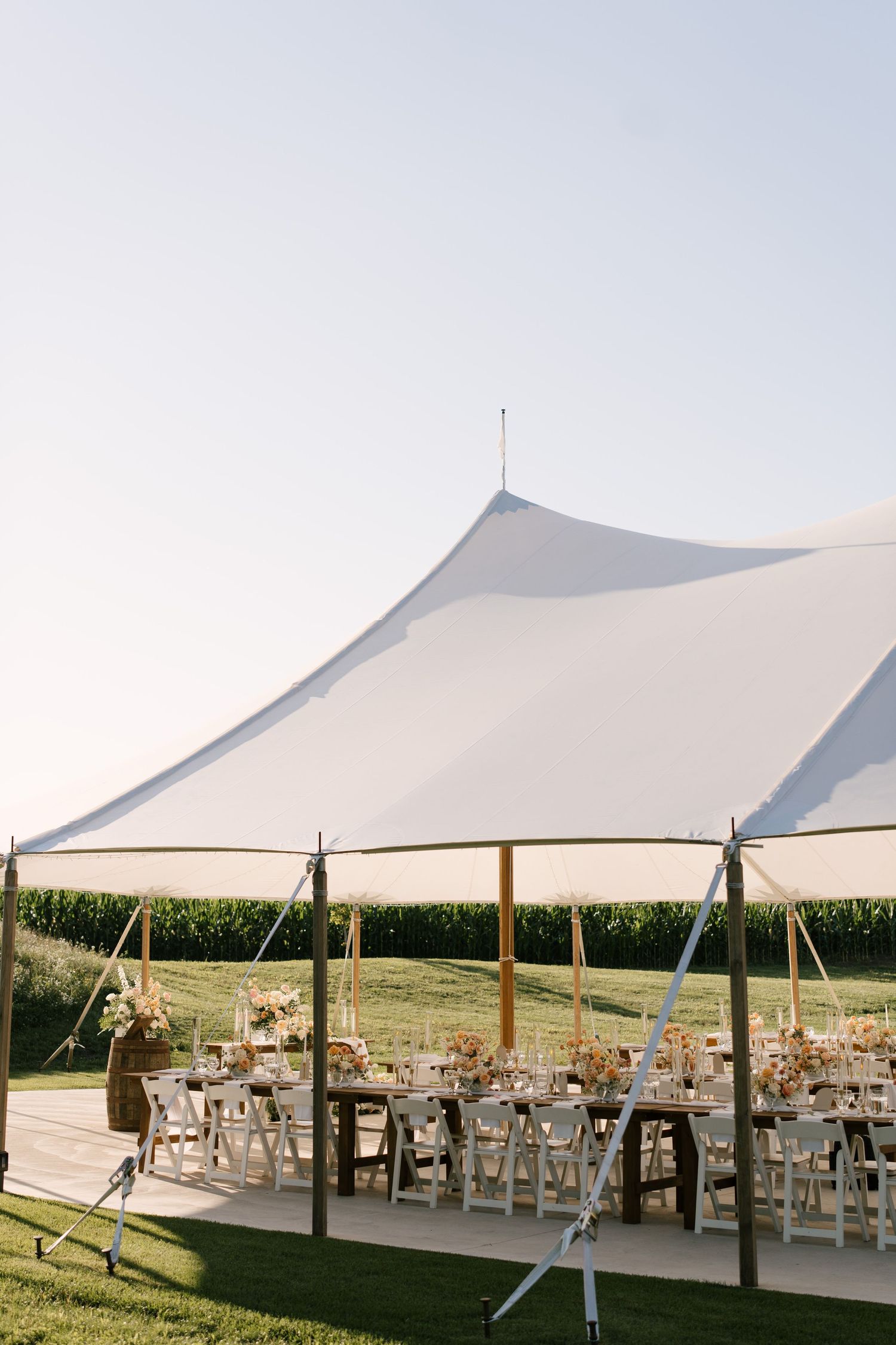 Outdoor Wakefield Estates wedding reception under a white sailcloth tent with rustic wooden tables and floral centrepieces.