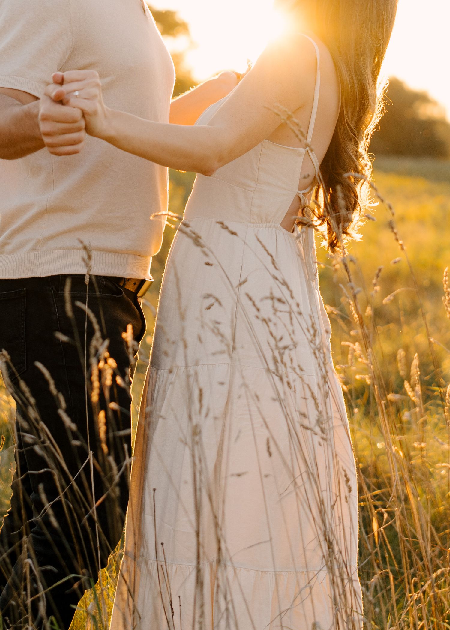 Close-up of couple holding hands and dancing together in a glowing sunset field.