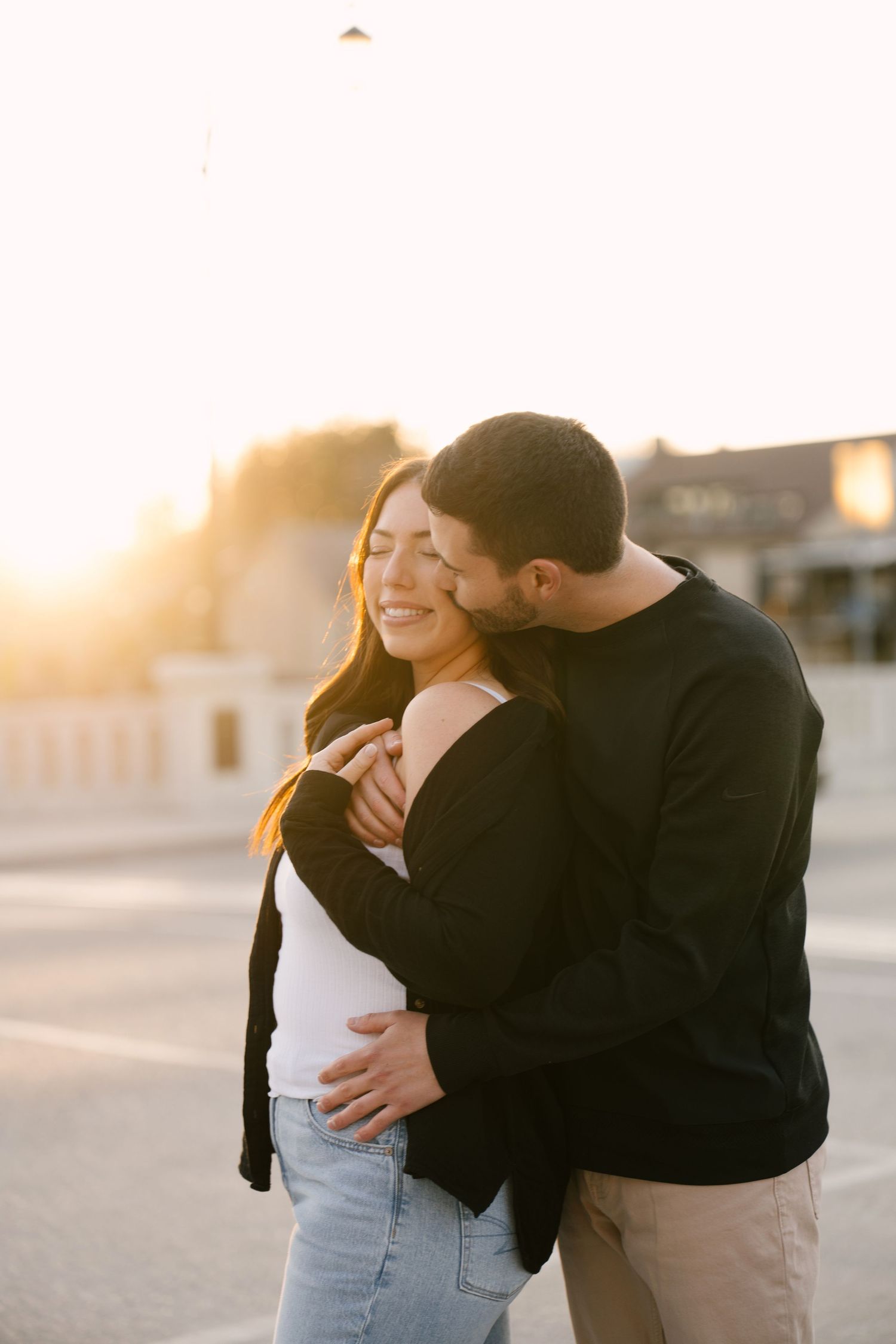 Man embracing woman from behind as they share a romantic moment in warm sunset light.