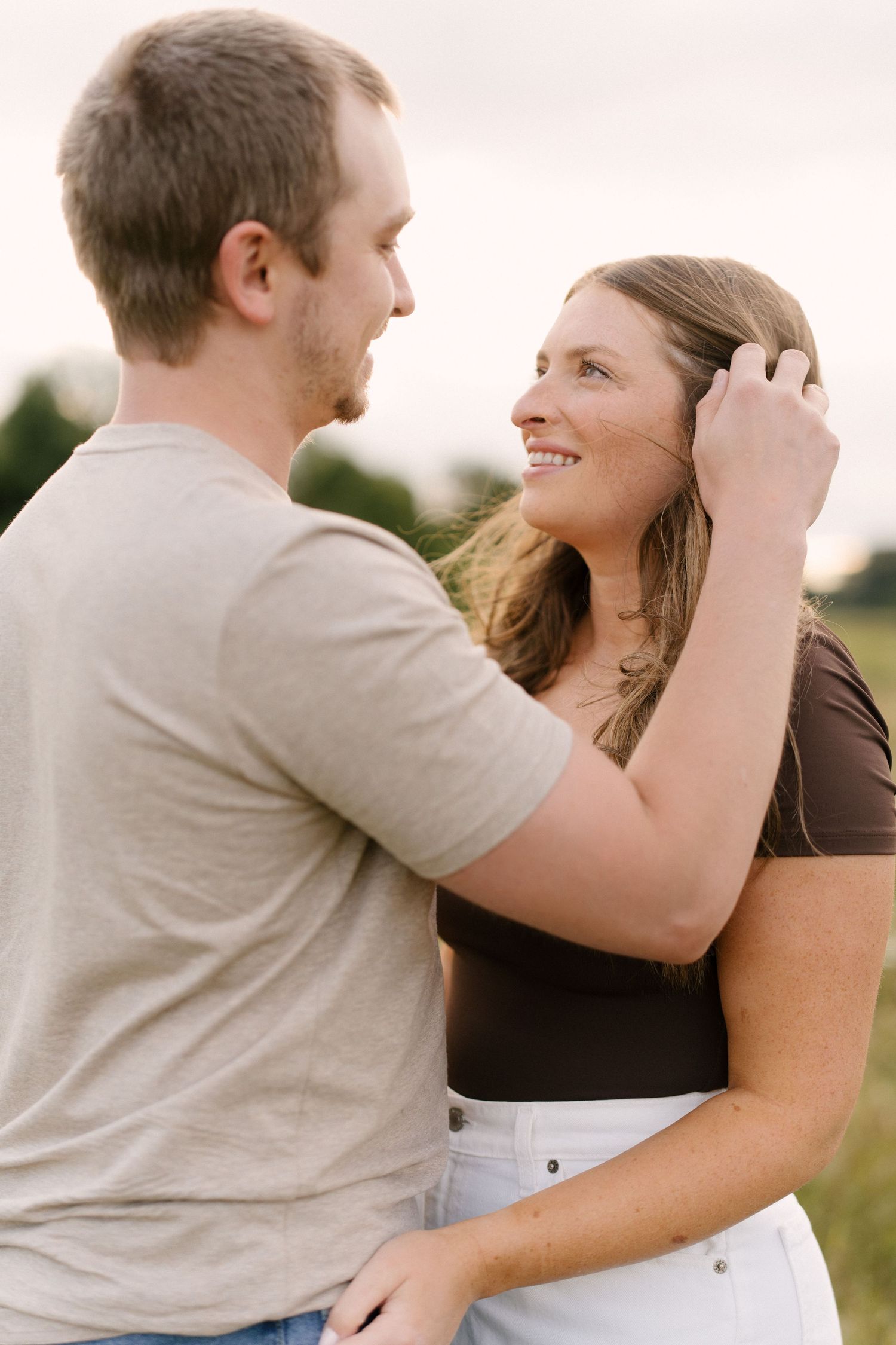 Man gently brushing woman's hair back while she smiles up at him in a field.