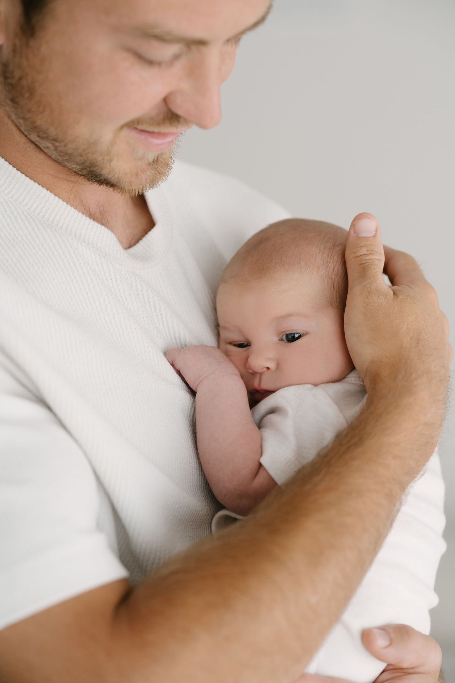 Close-up of father in white shirt cradling sleeping newborn baby against his chest.
