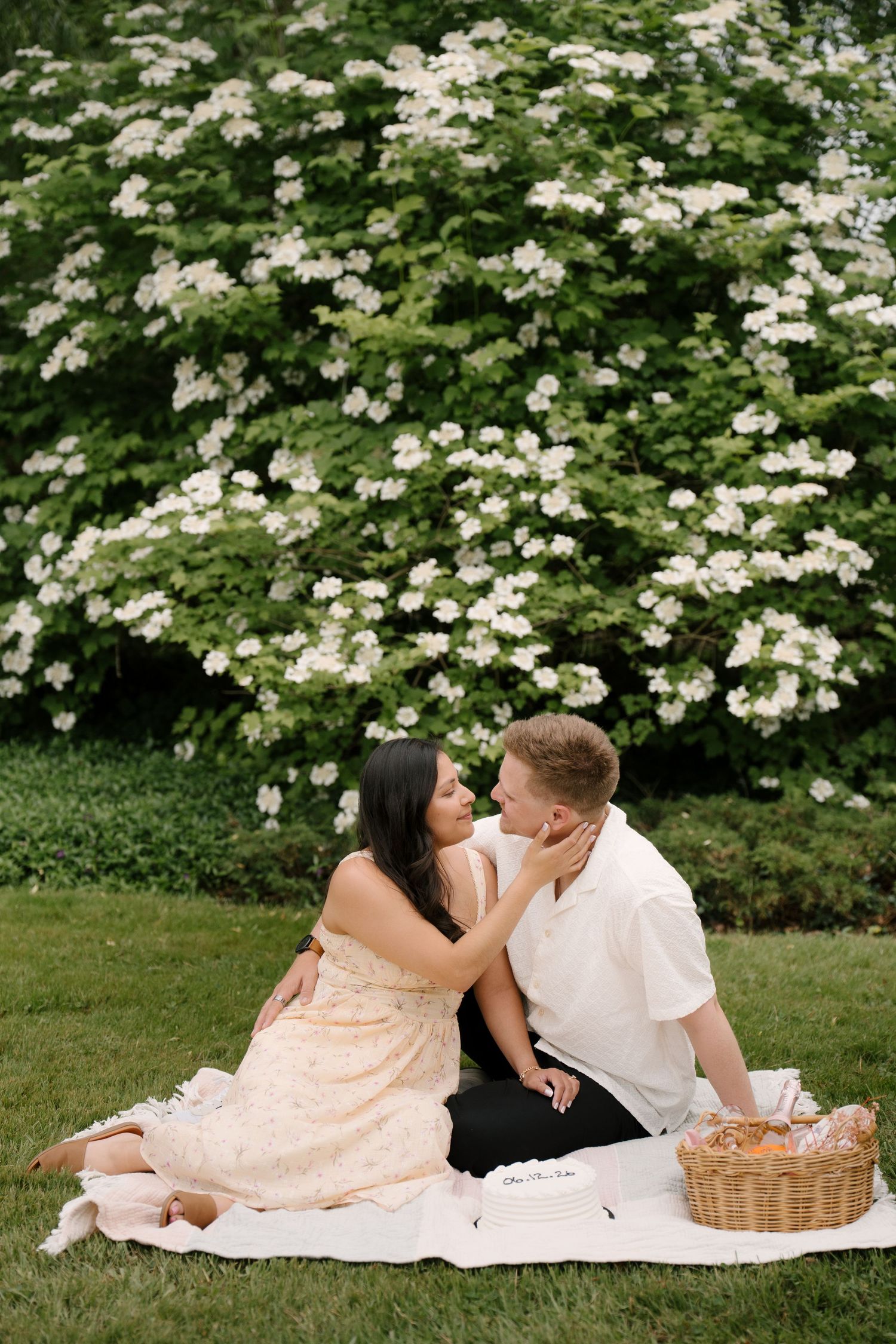 Couple sitting on a blanket near a blooming white flowering tree during a garden picnic.