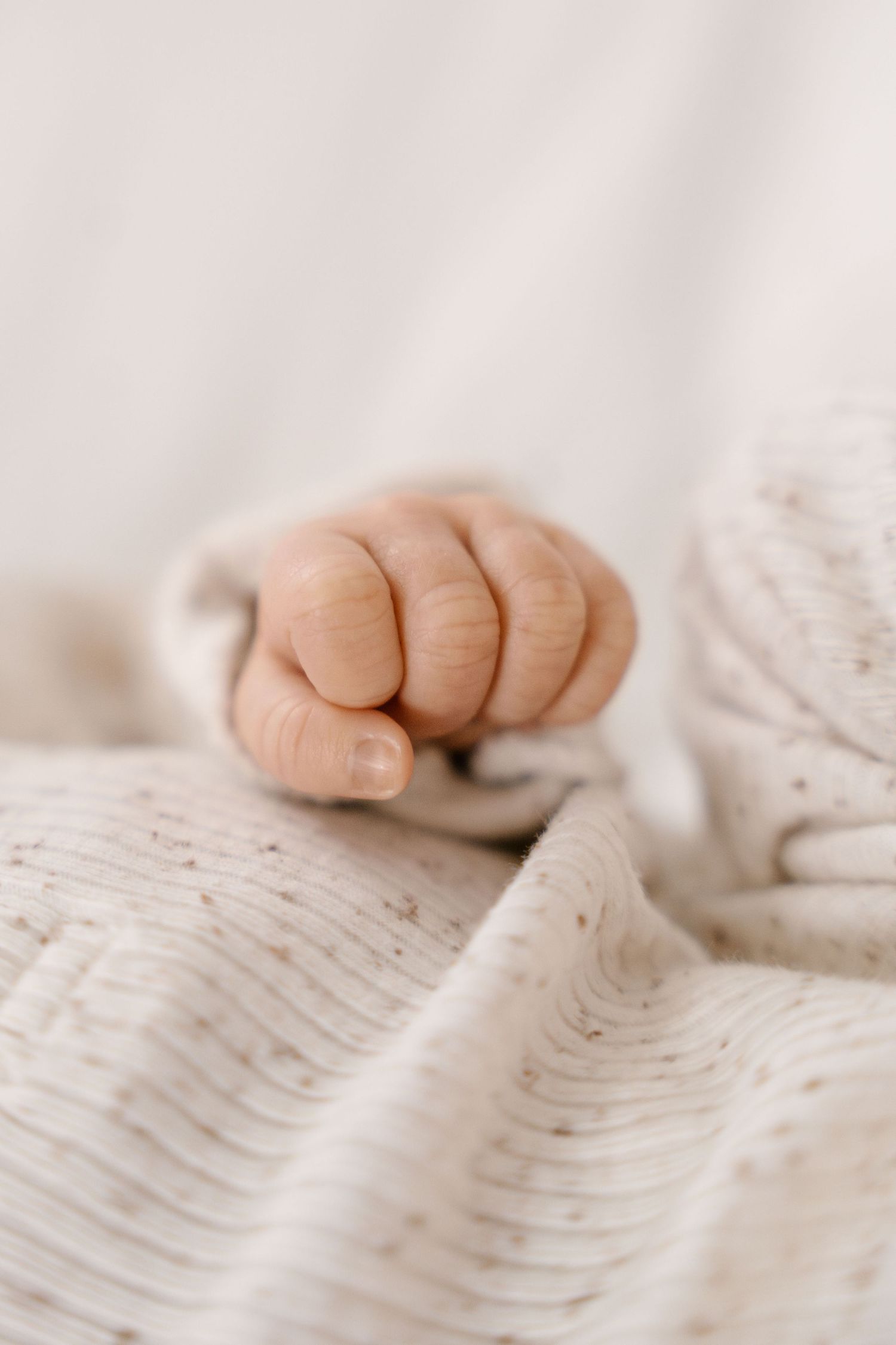 Close-up of sleeping newborn baby tiny fist resting on soft cream knit blanket.