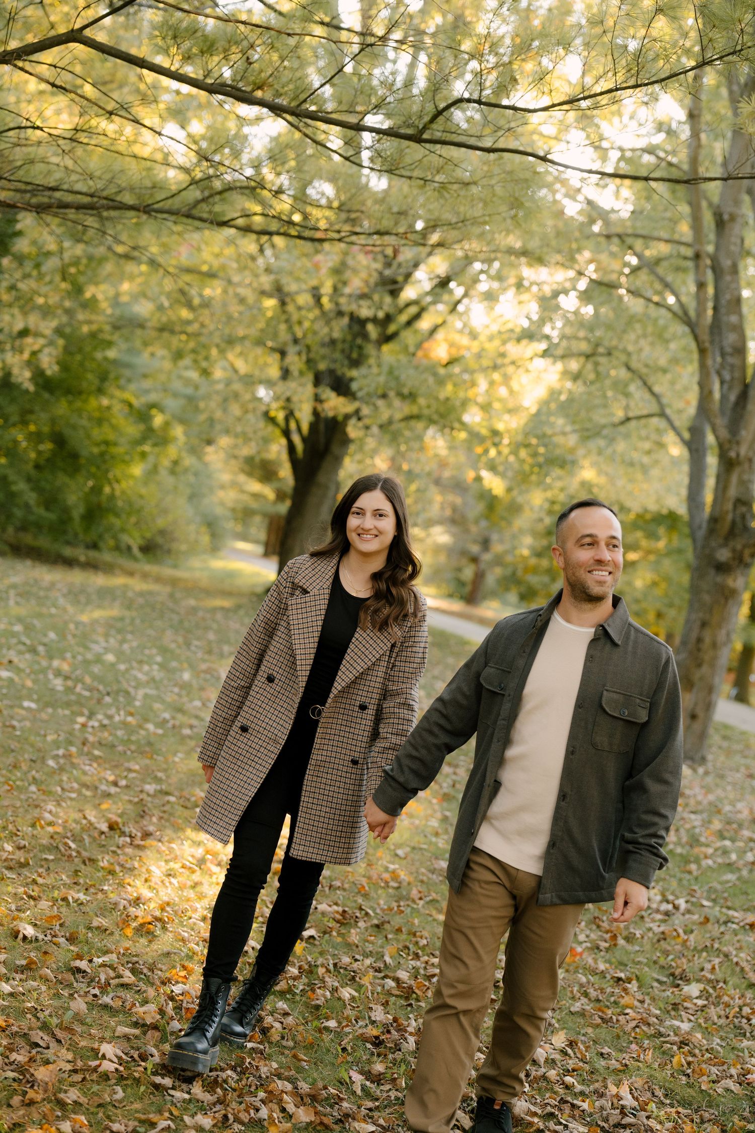 Smiling couple walking hand in hand through golden autumn park with fallen leaves.