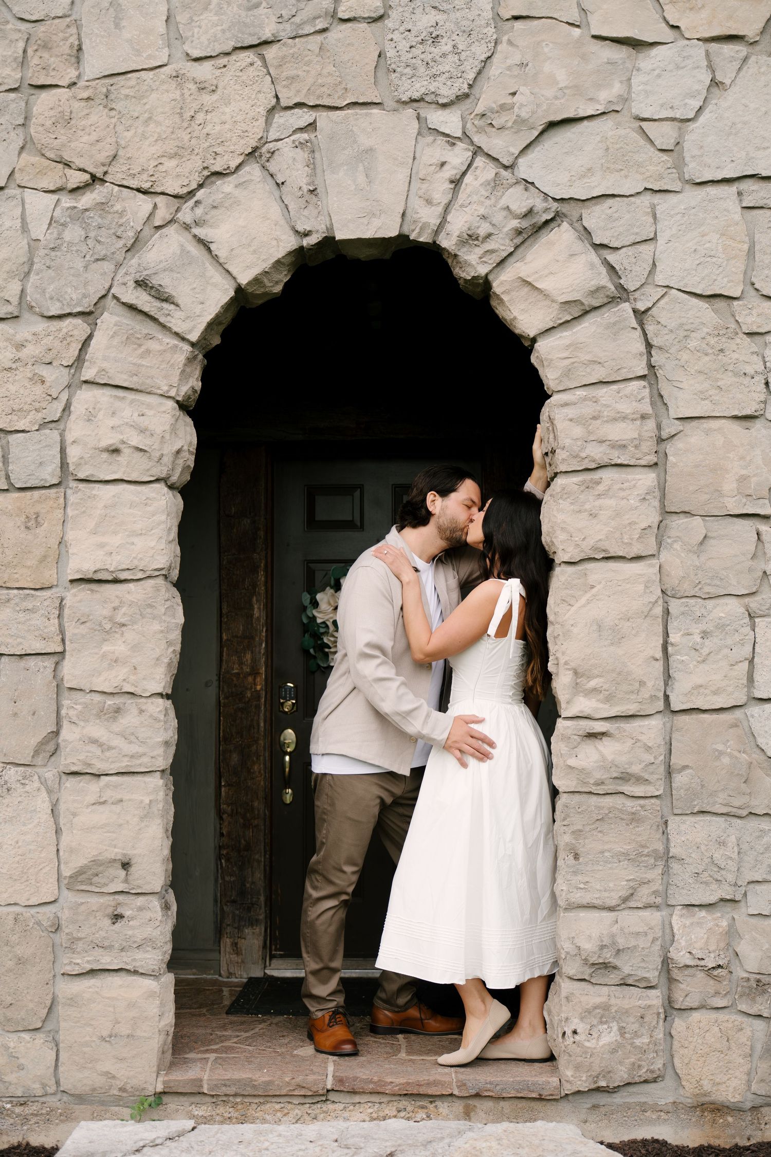 Couple sharing a kiss under a rustic stone archway doorway of a historic stone building.
