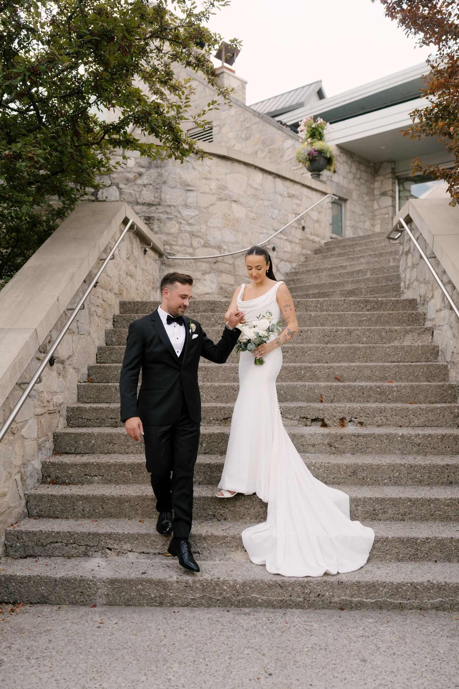 Bride and groom descend stone staircase hand-in-hand outside an elegant stone Cambridge Mill venue.