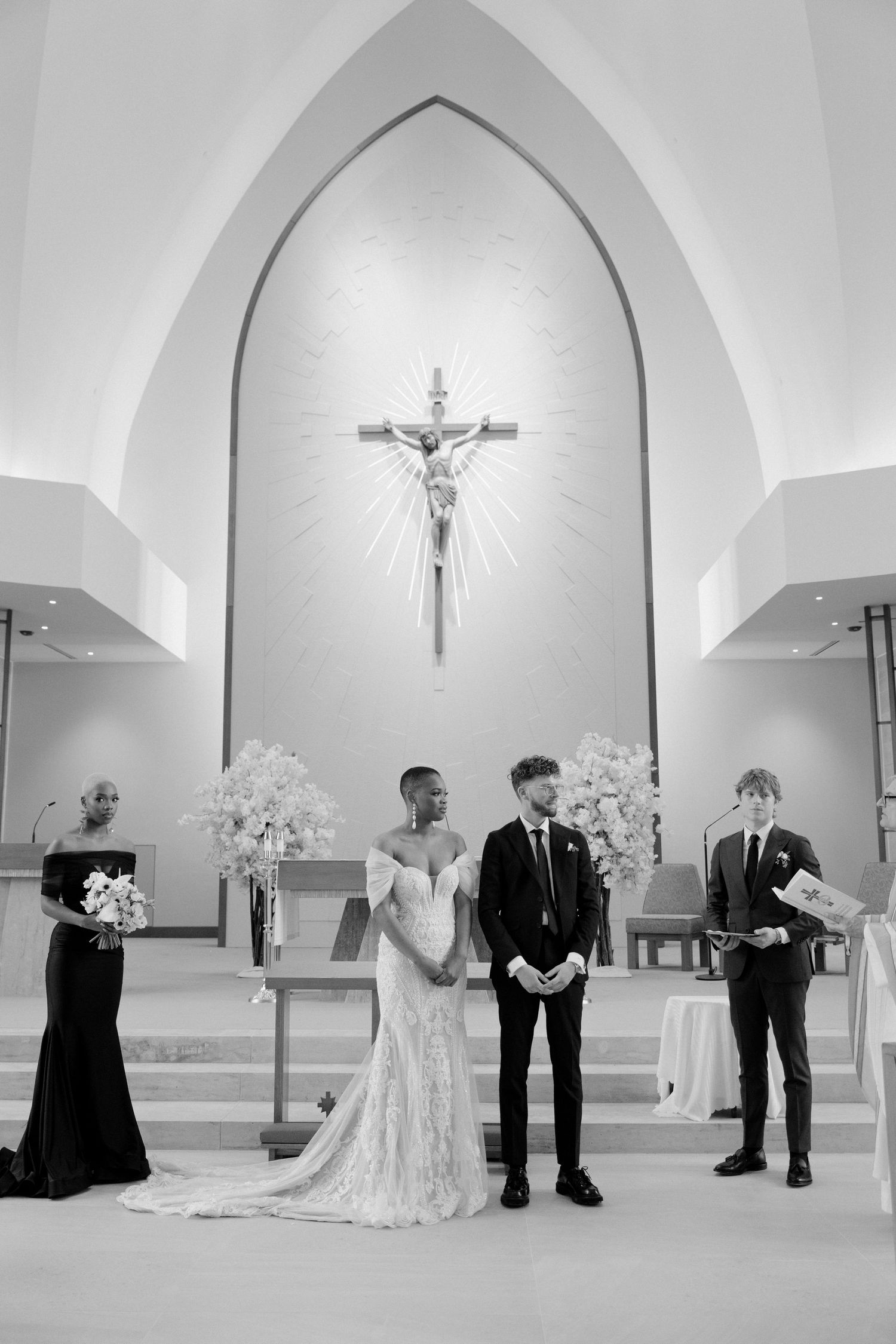 Black and white photo of bride and groom exchanging vows at church altar with crucifix backdrop.