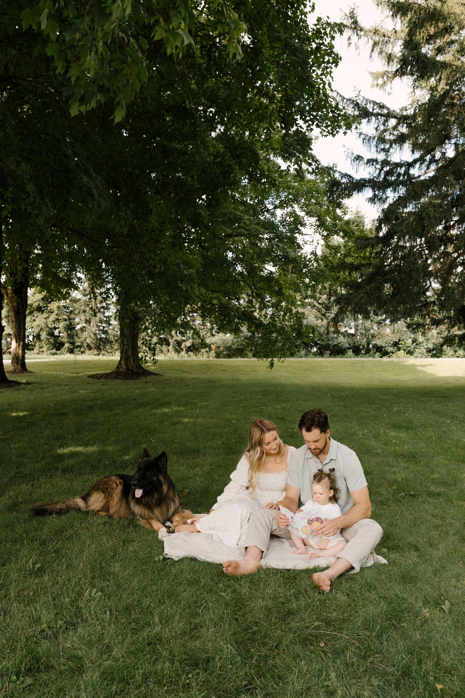 Family with baby and German Shepherd dog relaxing on blanket in park.