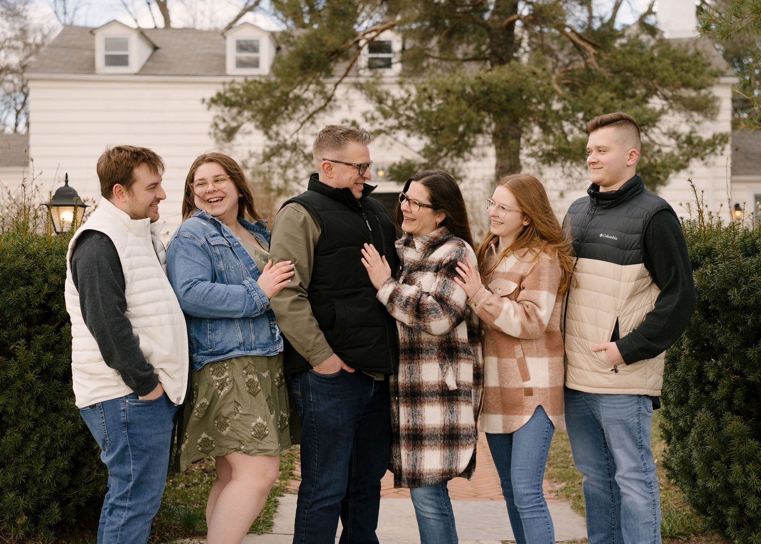 Happy family of six posing outdoors in front of a white house during a fall family portrait session.