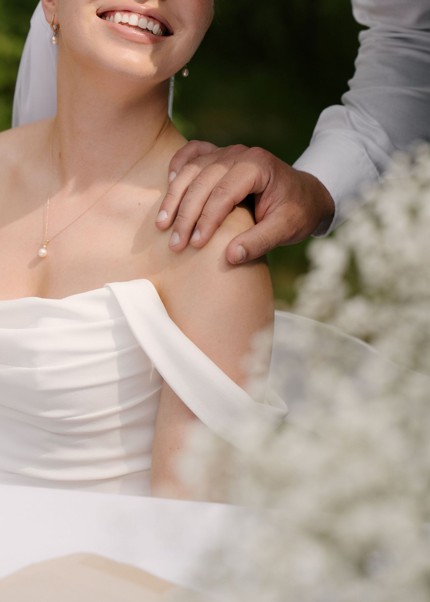 Groom gently places his hand on the bride's bare shoulder as she smiles during their wedding day.